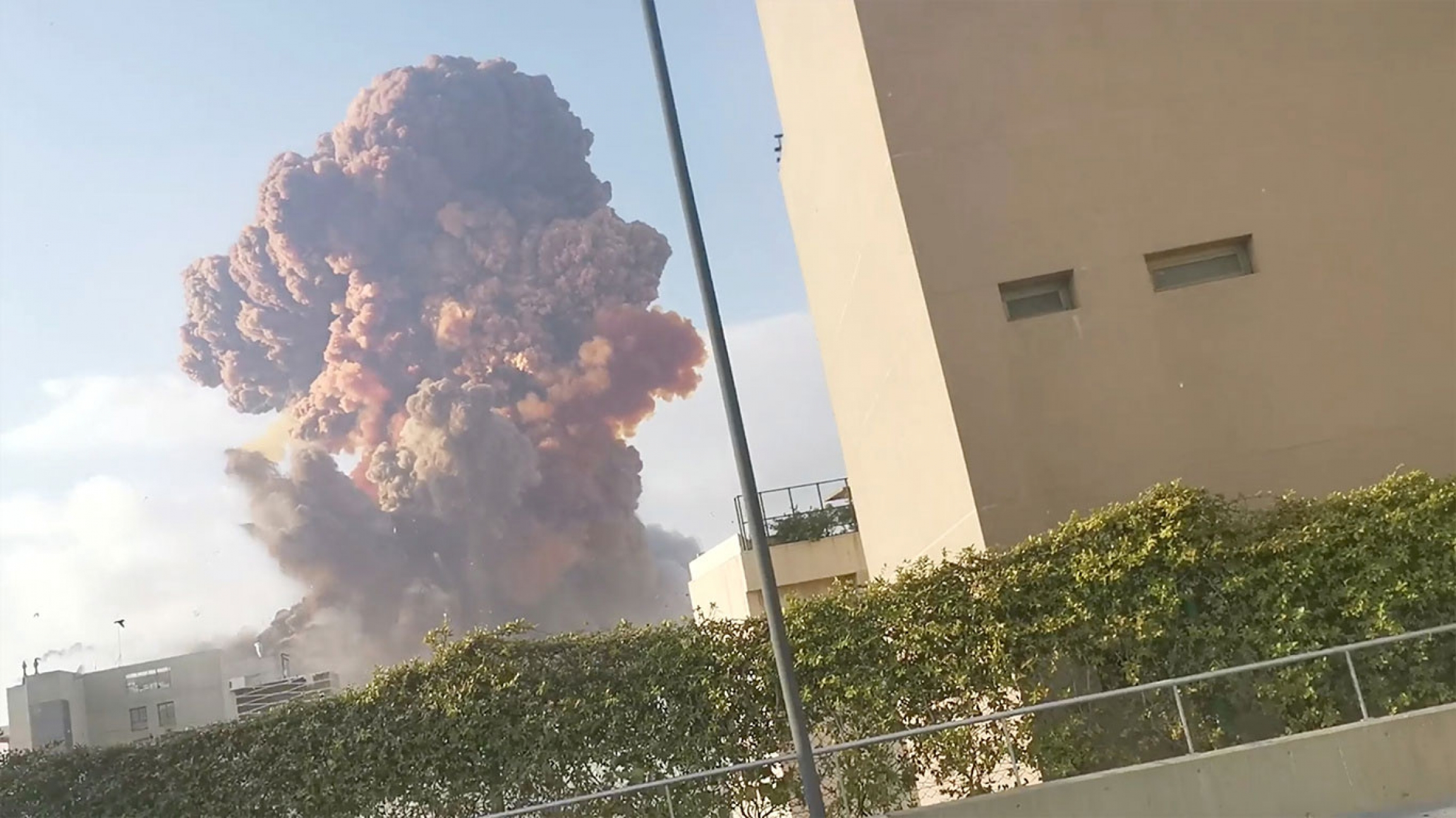Smoke rises after an explosion in Beirut, Lebanon August 4, 2020, in this picture obtained from a social media video. The dark plume of an explosion rises in the distance with a khaki-colored building in the nearground.