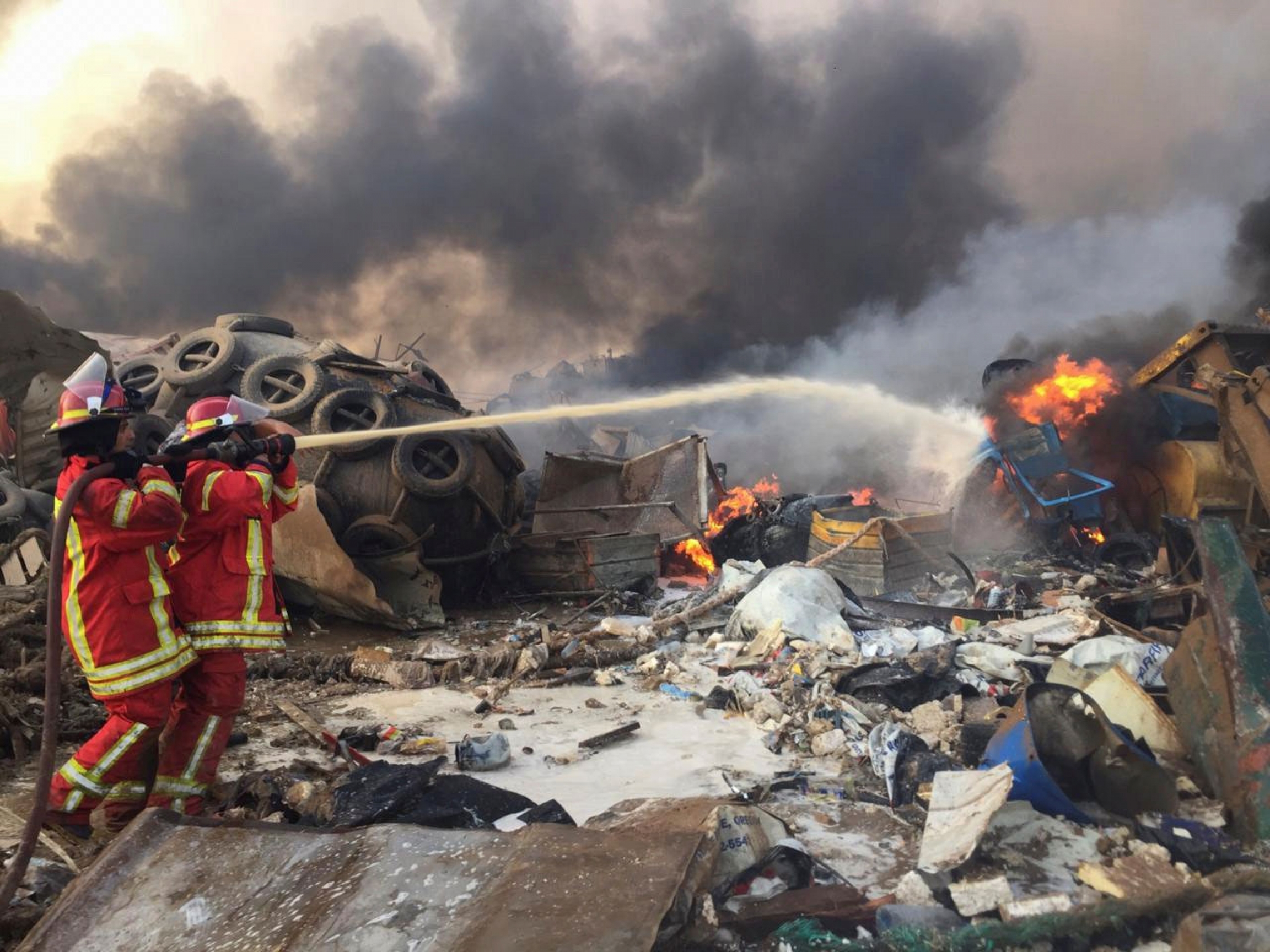 Firefighters spray water at a fire after an explosion in Beirut, Lebanon August 4, 2020. Two firefighters are shown holding a hose and spraying at a fire with building debris scattered everywhere.