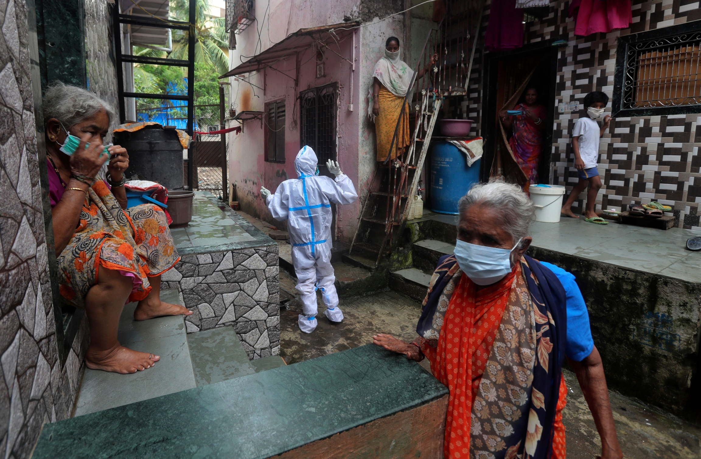 A health worker calls out to people to come out for screening for COVID-19 symptoms in Mumbai, India, Aug. 11, 2020. India has the third-highest coronavirus caseload in the world after the United States and Brazil. Several people are shown wearing brightly color saris with a peron center frame wearing a full protective medical outfit.