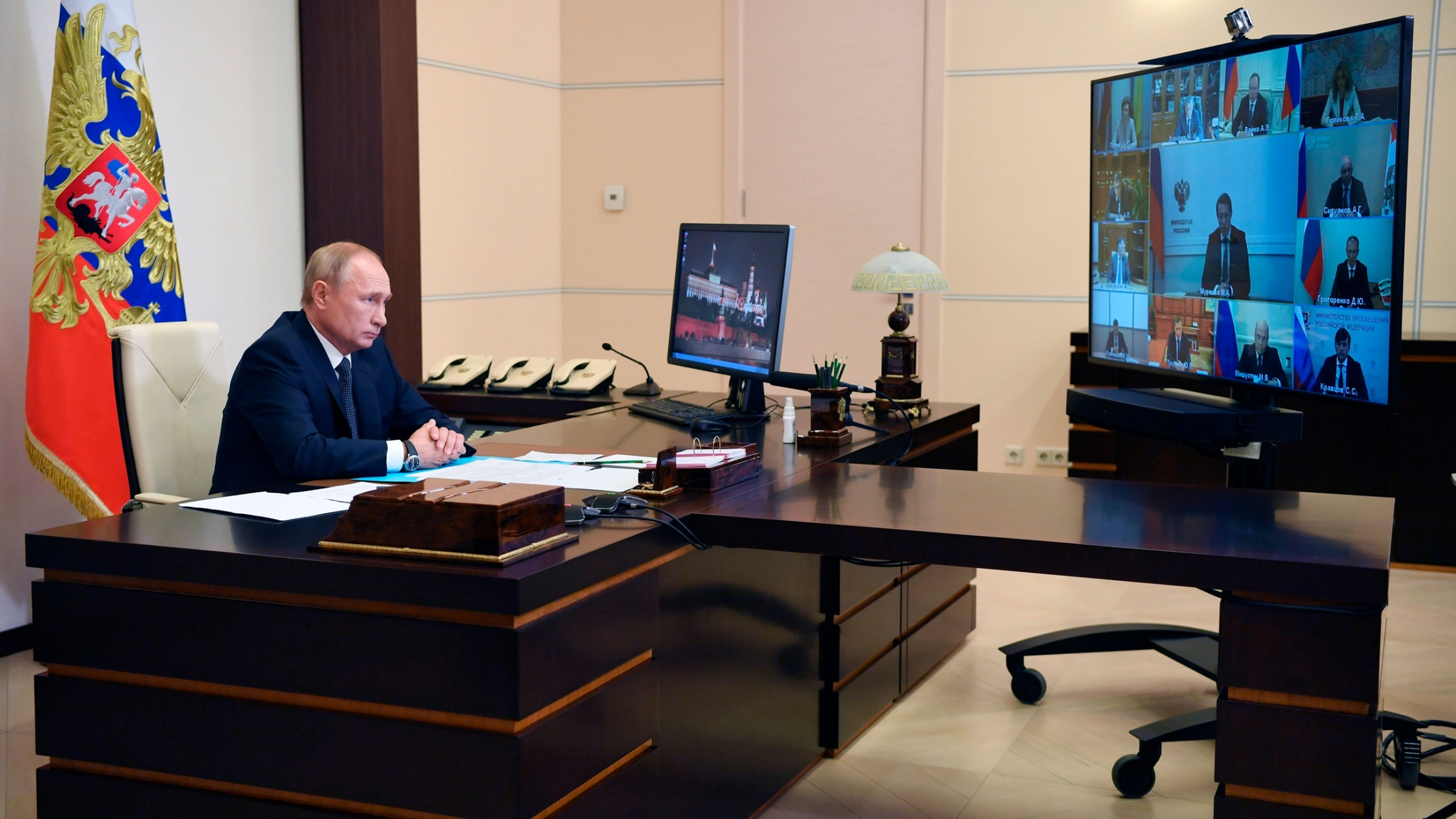 Russian President Vladimir Putin attends a cabinet meeting at the Novo-Ogaryovo residence outside Moscow, Russia, Tuesday, Aug. 11, 2020. Putin says that a coronavirus vaccine developed in the country has been registered for use and one of his daughters h Russian President Vladimir Putin attends a virtual cabinet meeting while sitting at a large wooden desk with a television monitor showing several officials.