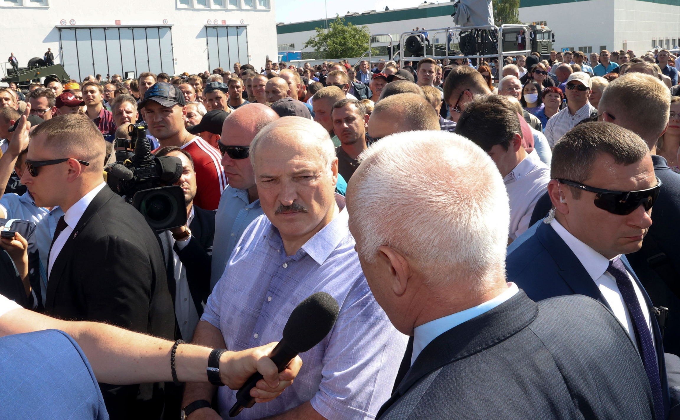 Belarusian President Alexander Lukashenko, center, surrounded by his bodyguards listens to an employee of the Minsk Wheel Tractor Plant in Minsk, Belarus, Monday, Aug. 17, 2020. Belarusian President Alexander Lukashenko is shown wearing a blue button down shirt and standing in a large crowd with bodyguards surrounding him.