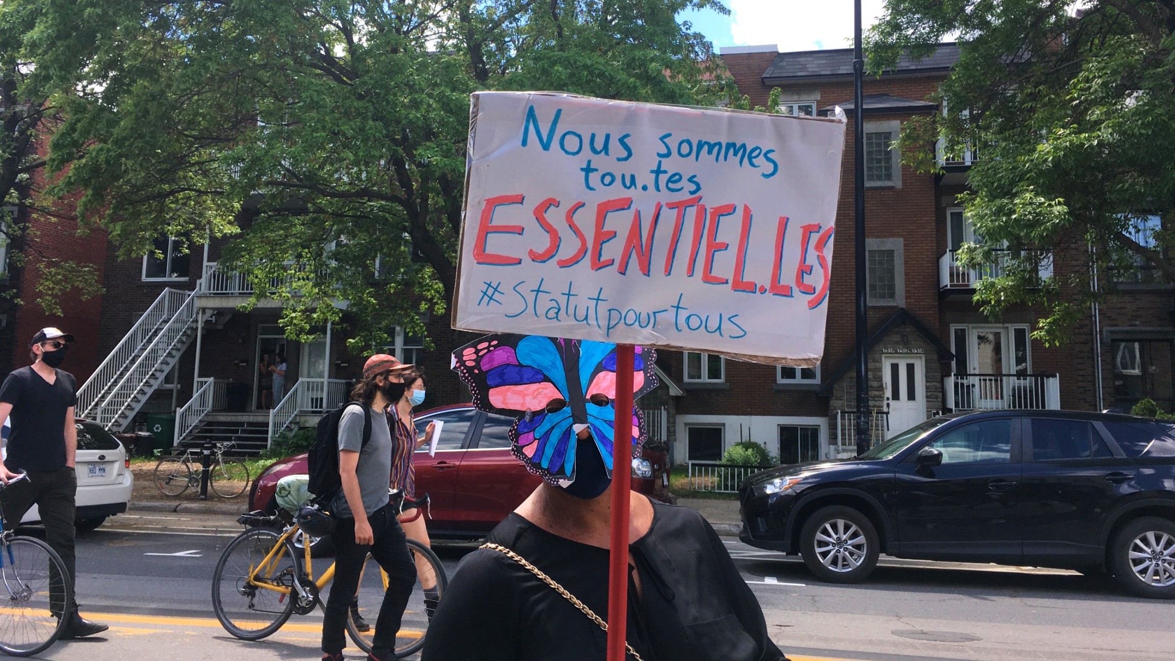 A demonstrator in Montreal holds up a sign in French saying, "We are all essential, status for all." A demonstrator in Montreal holds up a sign in French saying, "We are all essential, status for all."