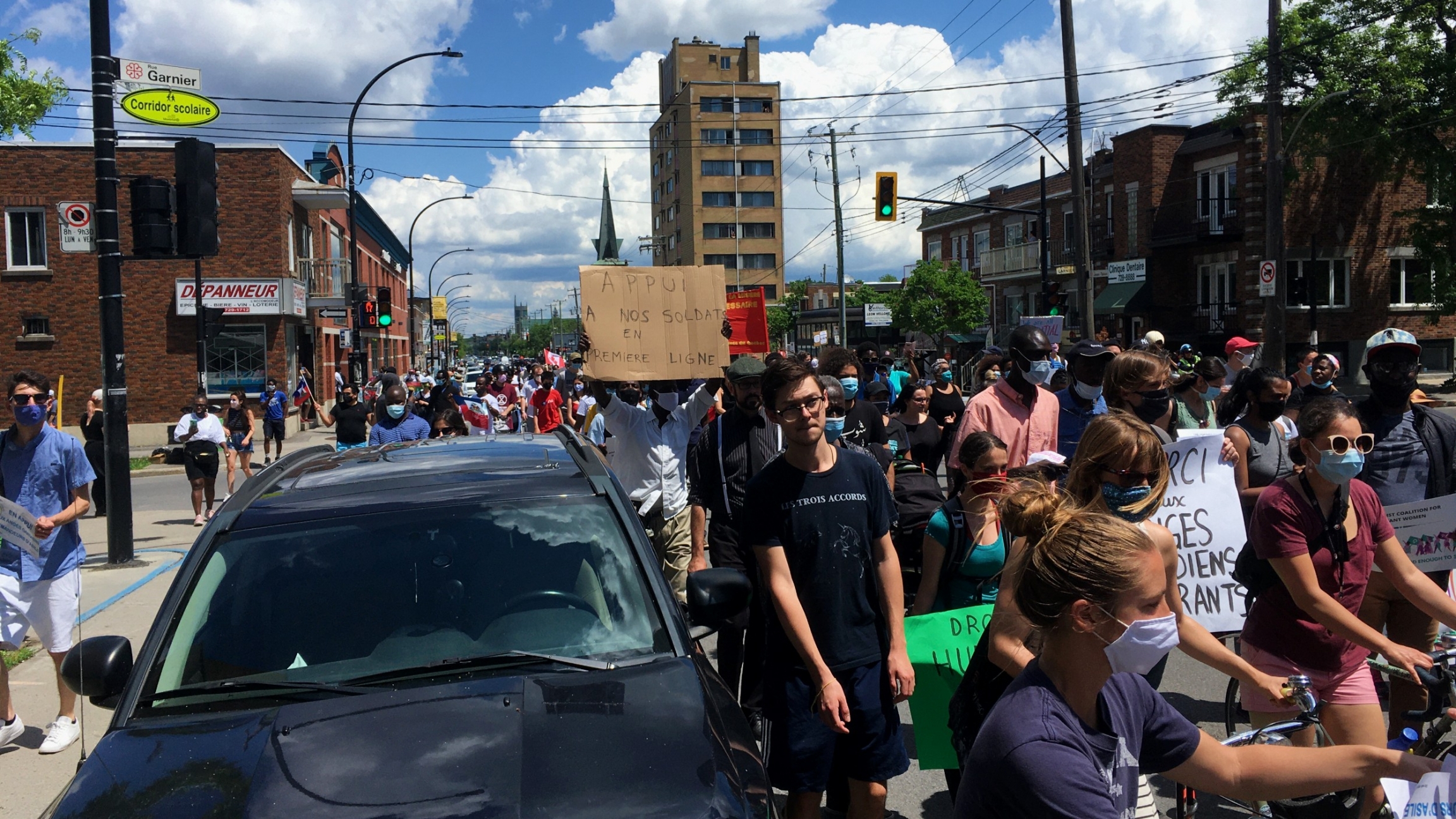 Protesters marching in Montreal hold up signs referring to "support for our soldiers on the frontlines," "Thank you to the immigrant guardian angels" and "Human rights for the guardian angels." Protesters stand in the street holding signs with slogans