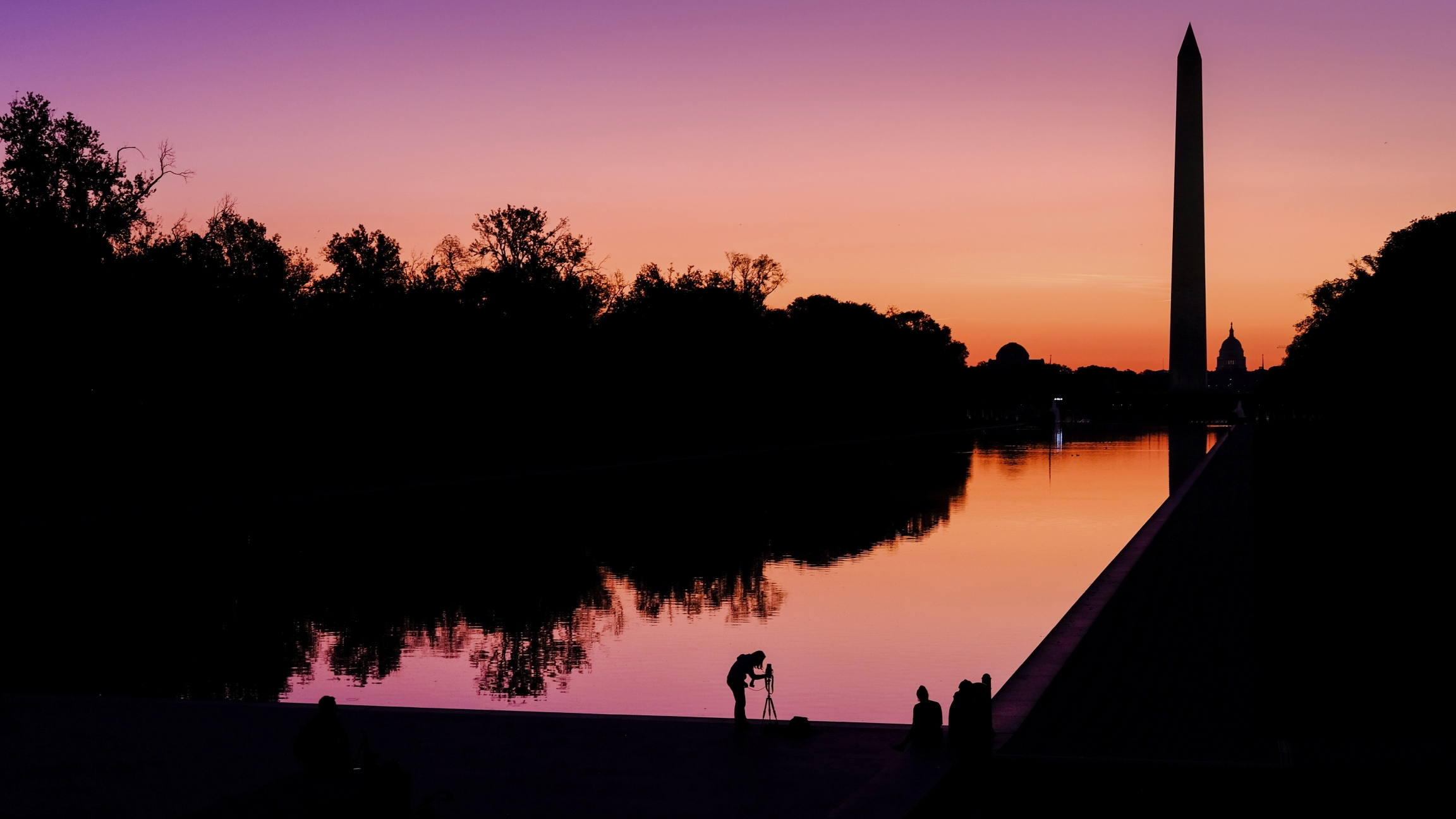 A photographer lines up her shot at the National Mall reflecting pool as the sun begins to rise behind the Washington Monument and the US Capitol building in Washington, Sept. 21, 2019. A pink and orange sunset along the National Mall in Washington DC with silhouetted trees