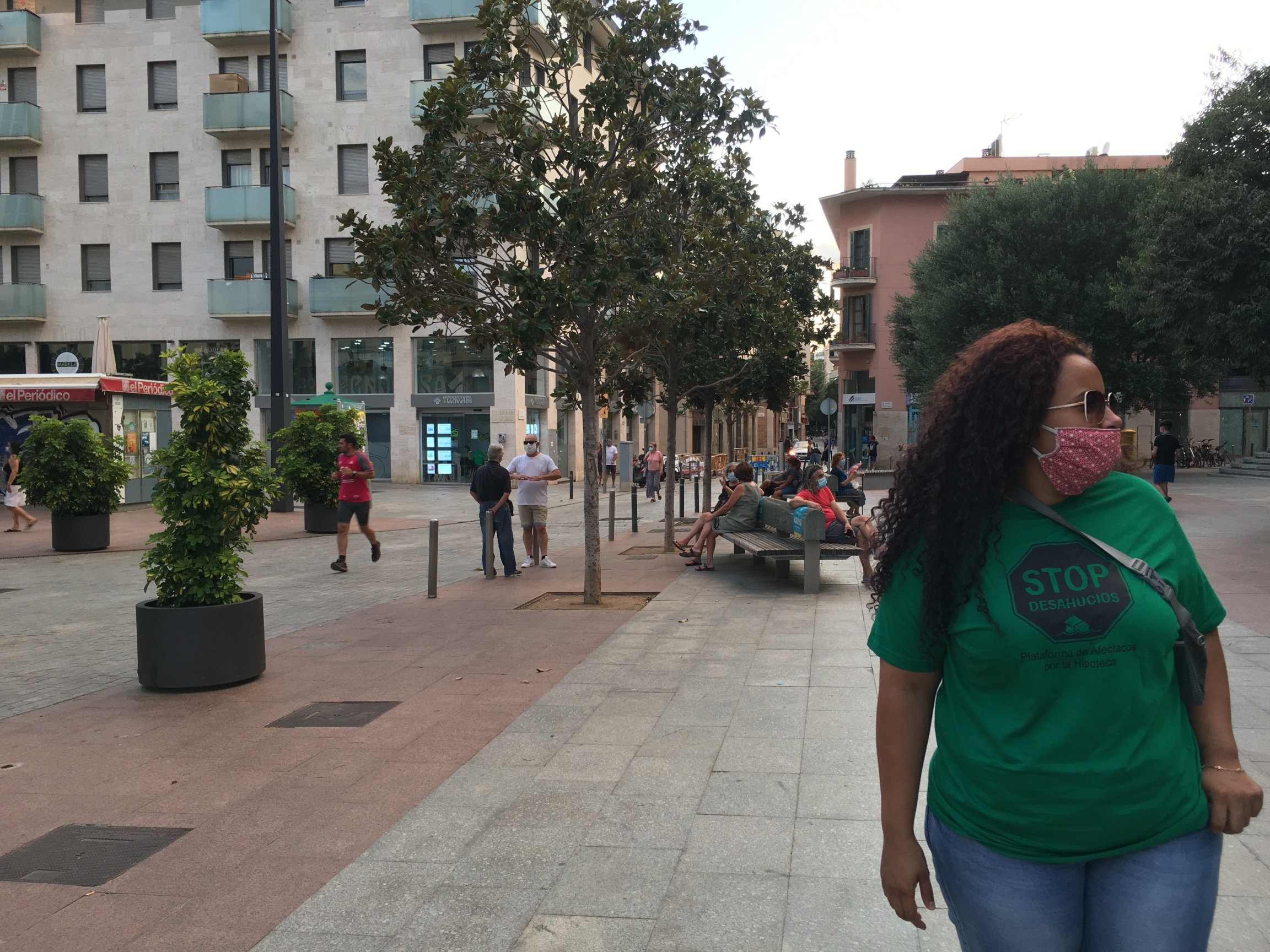 Marly Estrella lives with her two young children and husband in L’Hospitalet de Llobregat, a city bordering Barcelona that’s well-connected to the Catalan capital and relatively cheaper. But she could be evicted any day. A woman with long brown, curly hair wears a green shirt and jeans as she walks down an urban street.