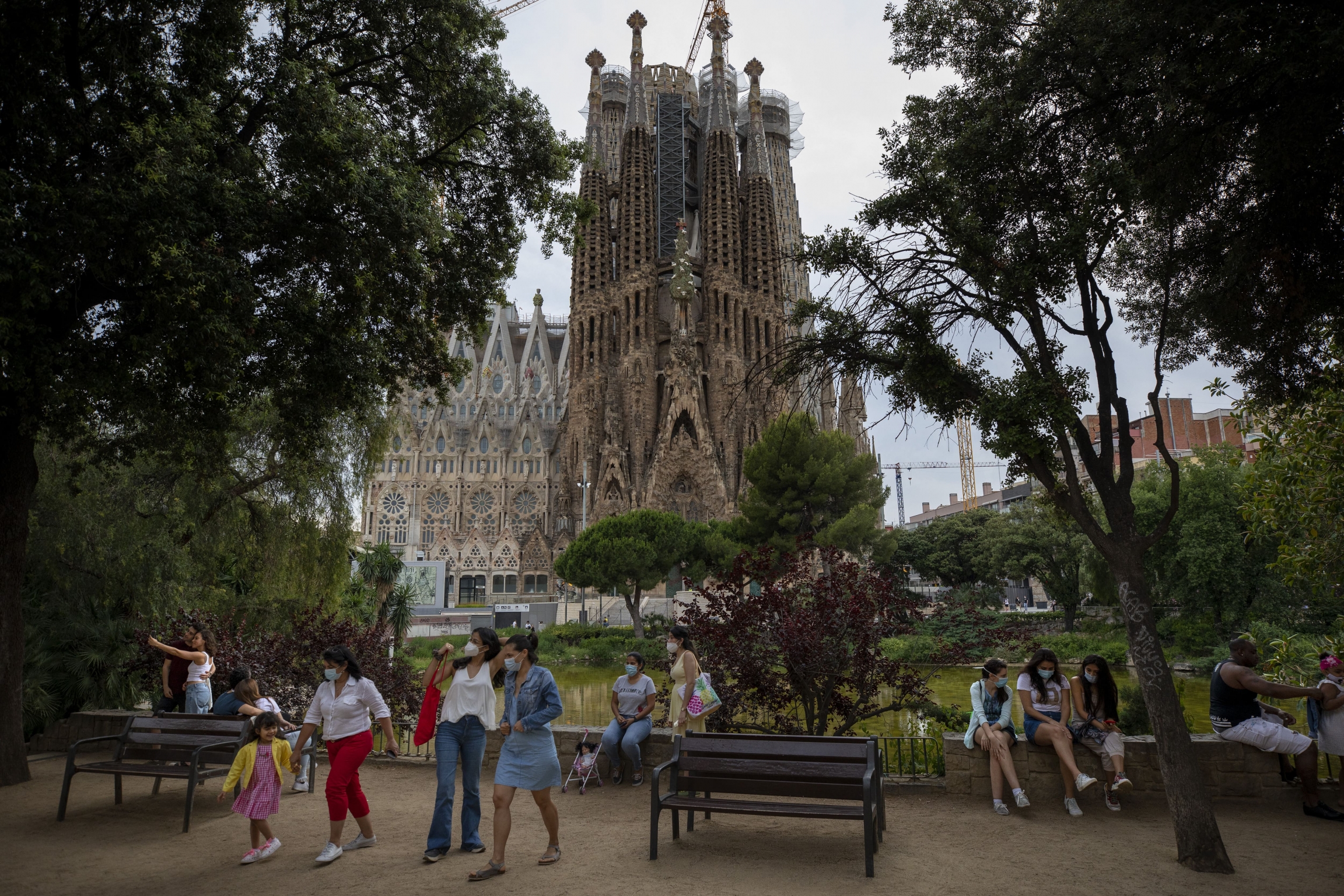 In this Sunday, May 31, 2020 file photo, local visitors enjoy a park next to the Antoni Gaudí's La Sagrada Familia Basilica in Barcelona. Barcelona’s iconic La Sagrada Familia basilica has reopened its doors for visits exclusively for health workers after People wearing face masks stand and sit outside a large, ornate church.