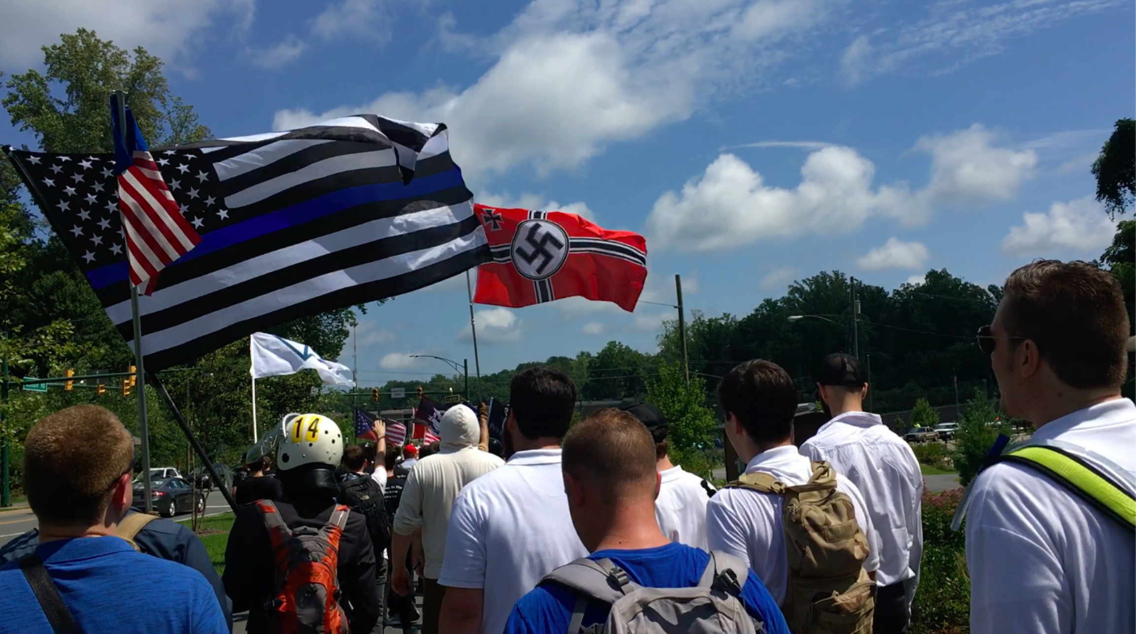 Screenshot of video footage of a white power rally in Chartlottesville, Virginia, taken by Patrik Hermansson, who went undercover with far-right groups in the US for one year. White men walk down a street with white power flags showing Nazi symbols