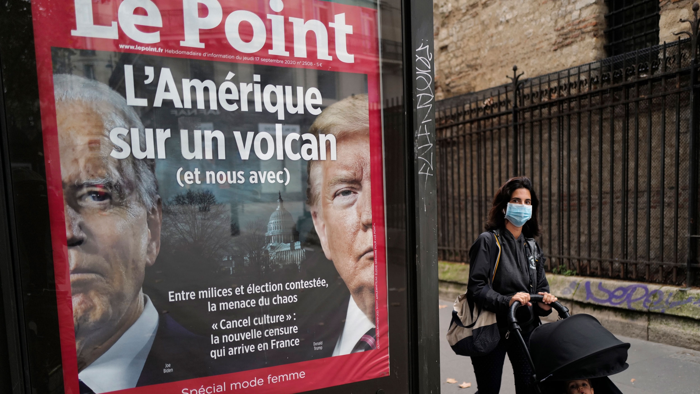 The front page of French weekly newspaper Le Point displays a photo of President Donald Trump and Democratic presidential candidate former Vice President Joe Biden with a headline reading, "America on a volcano, (and us, too)," in Paris, Sept. 30, 2020. A small billboard for the French publication, Le Point, is show with the faces of Donald Trump and Joe Biden on it and a woman is shown walking past.