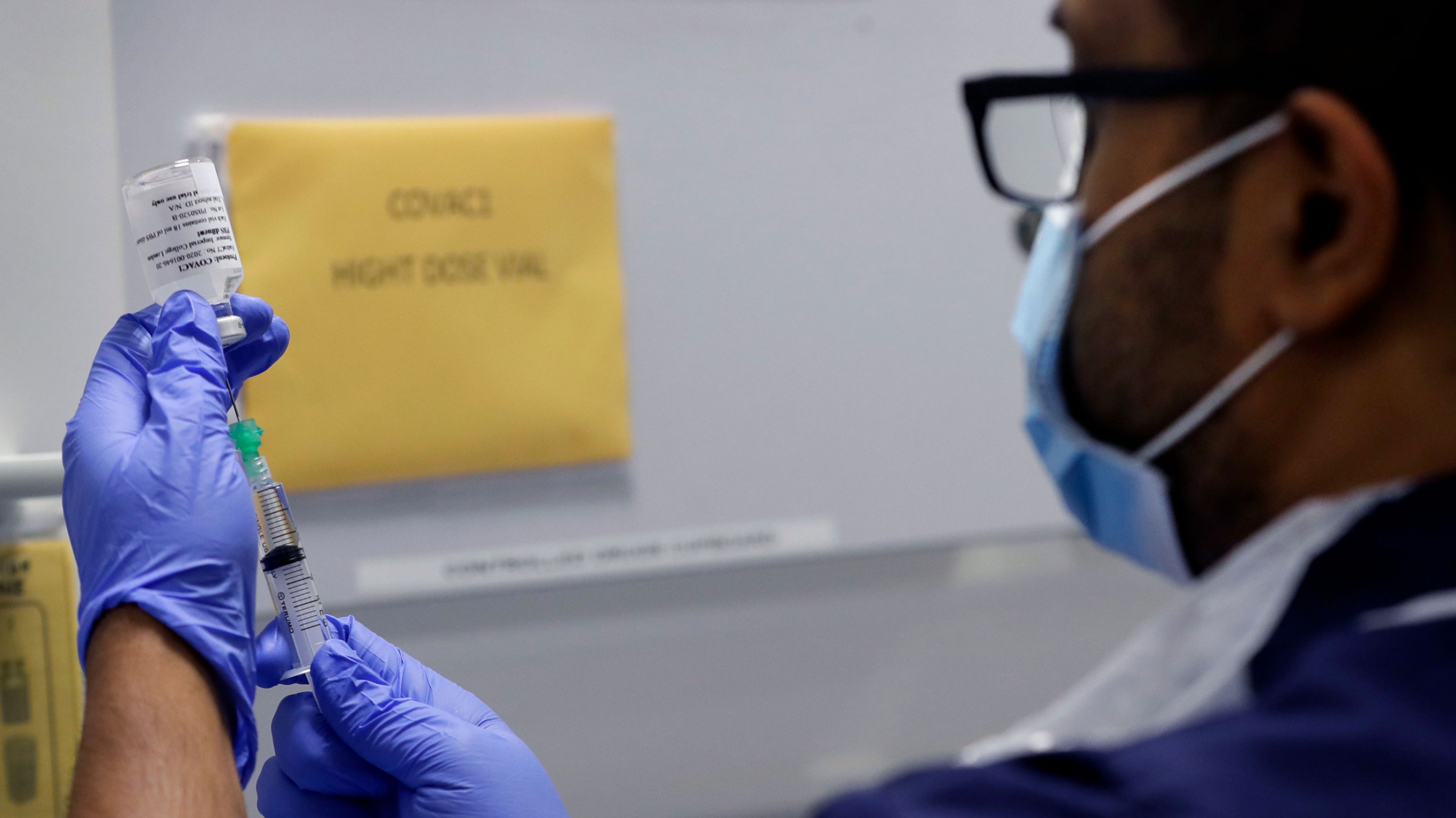 Senior Clinical Research Nurse Ajithkumar Sukumaran prepares the COVID-19 vaccine to administer to a volunteer, at a clinic in London. A nurse is shown wearing glasses and face mask while holding with both hands a syrine and vaccine dose bottle.