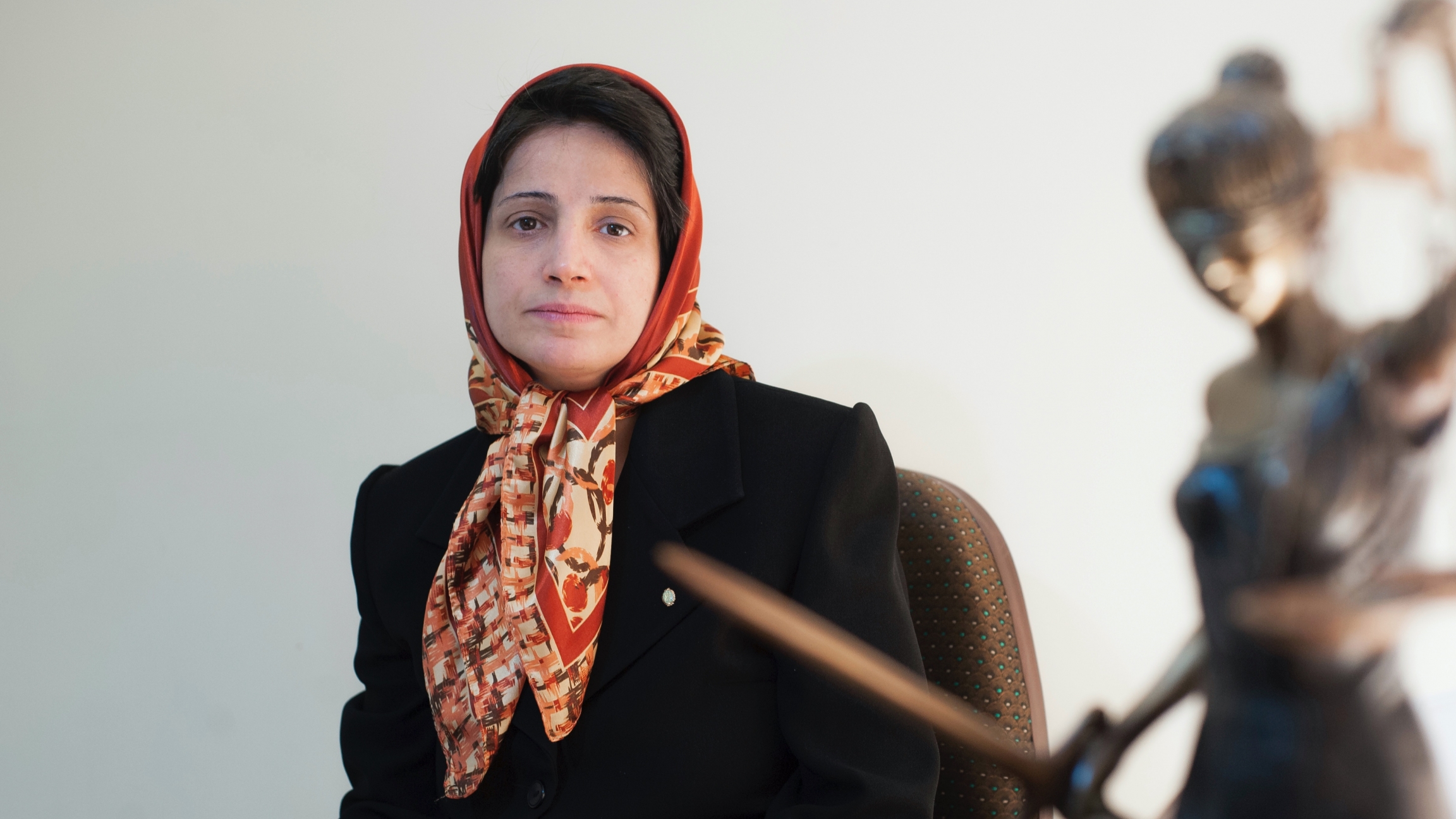 A woman wearing a head scarf sits at her desk and poses for a photograph. 