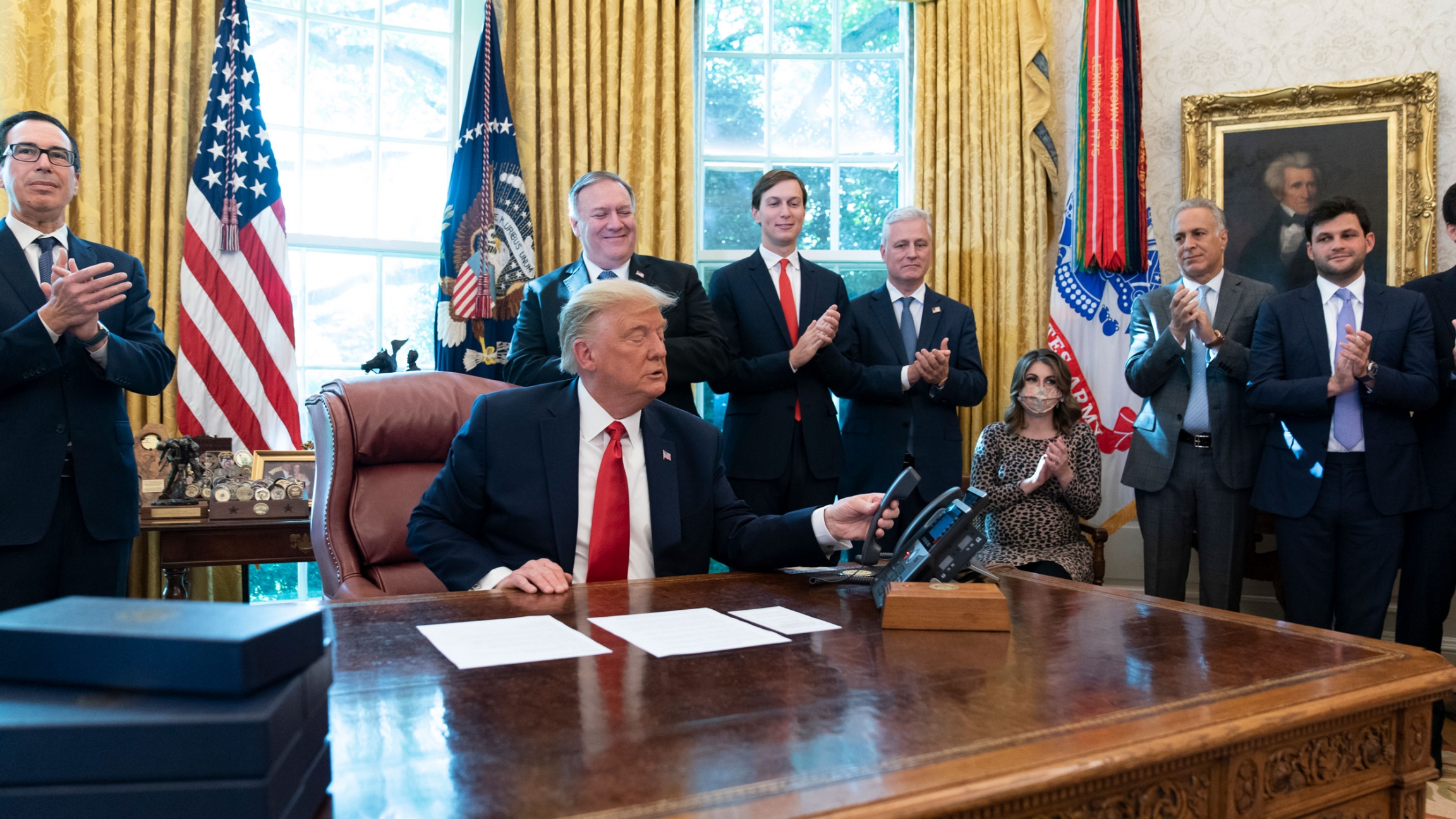 US President Donald Trump hangs up a phone call with the leaders of Sudan and Israel in the Oval Office of the White House, Oct. 23, 2020. Donald Trump is shown sitting at a desk and wearing a dark suit with a red tie and hanging up a phone.