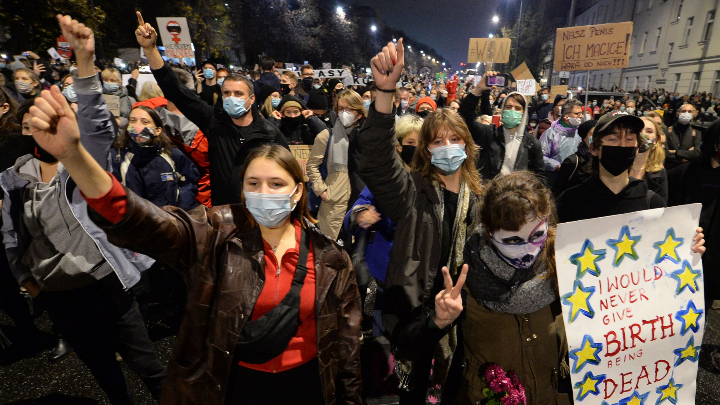 A crowd gathers outside the house of Poland's ruling conservative party leader Jaroslaw Kaczynski protesting a court ruling that declared abortions of fetuses with congenital defects unconstitutional, Warsaw, Poland, Oct. 23, 2020. A large crowd of people are show in the street — many wearing protective face masks and carrying signs.