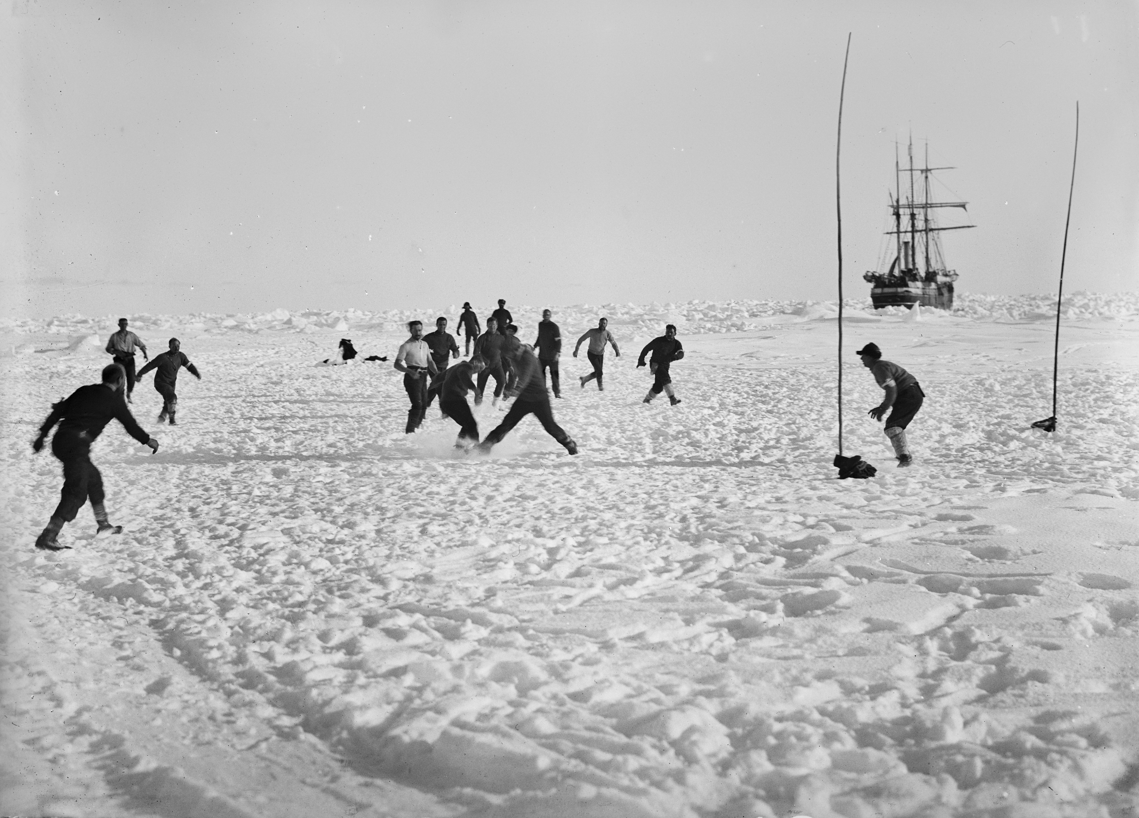 While The Endurance ship was trapped in sea ice along the Weddell Sea, men on board remained optimistic, seen here playing soccer in the snow. Men play soccer in white, snowy field nearby stuck ship