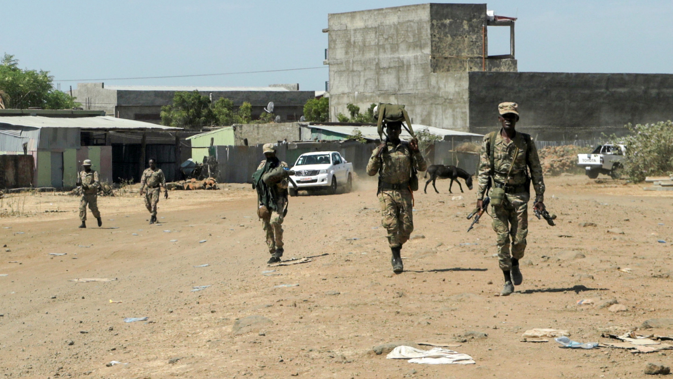 Members of the Amhara Special Force return to the Dansha Mechanized 5th division Military base after fighting against the Tigray People's Liberation Front, in Danasha, Amhara region near a border with Tigray, Ethiopia, Nov. 9, 2020. A small group of soldiers are shown walking and carrying weapons with a large cement structure in the distance.