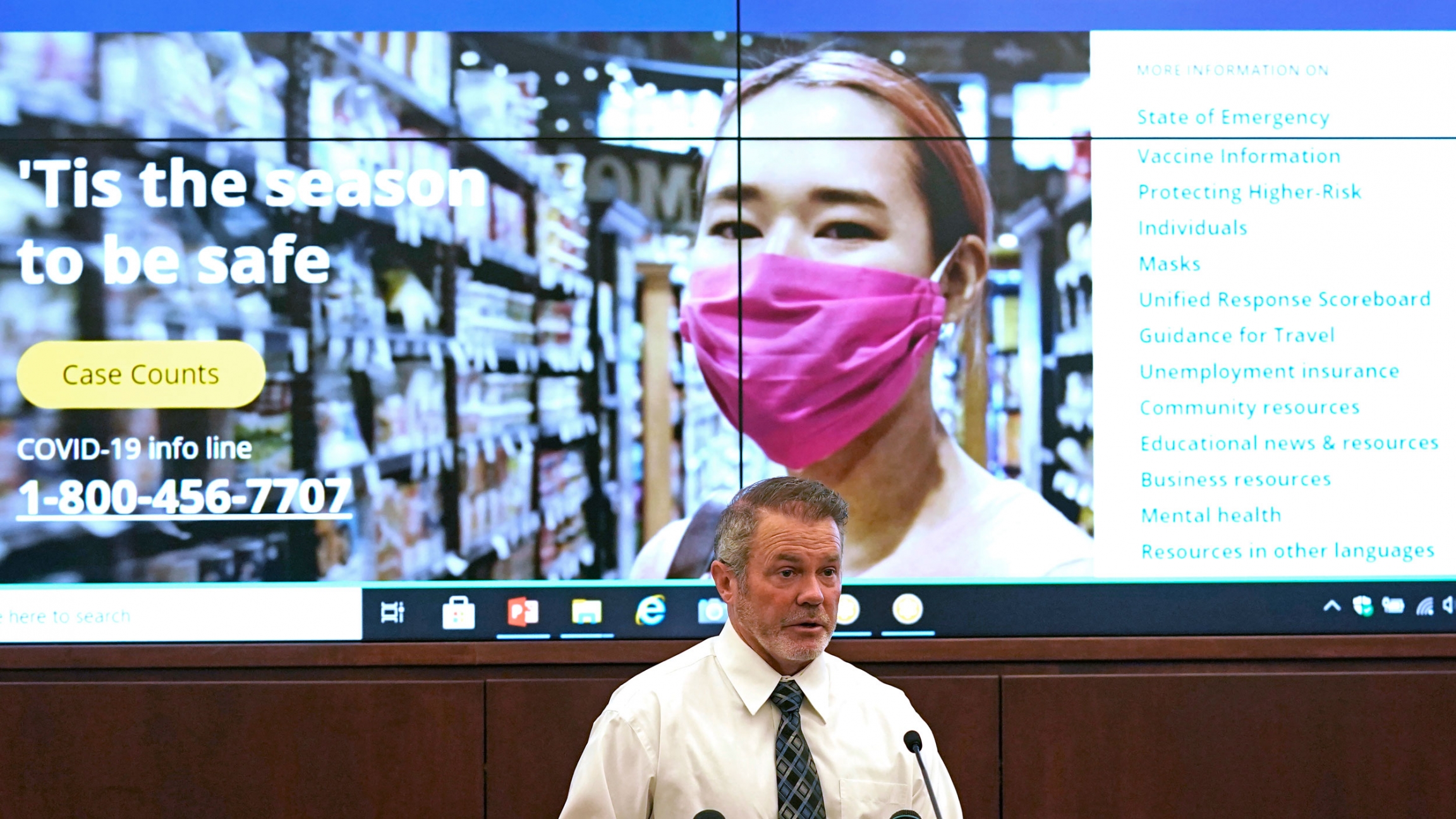 Rich Lakin, immunization program manager for the state health department, speaks during a news briefing, Nov. 18, 2020, in Salt Lake City. Health officials say Utah could receive its first round of a coronavirus vaccine as early as mid-December. A man wearing a white shirt and gray tie is shown speaking a t podium with a screen behind him showing promotional material on coronavirus safety.