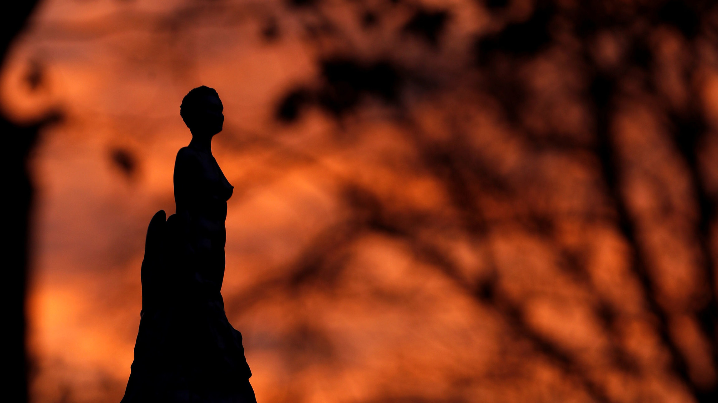 The silhouetted Mary Wollstonecraft statue by artist Maggi Hambling, is pictured in Newington Green, London, Britain, Nov. 11, 2020. The dark silhouetted of a statue is shown with the orange and red colors of a sunset in the distance.