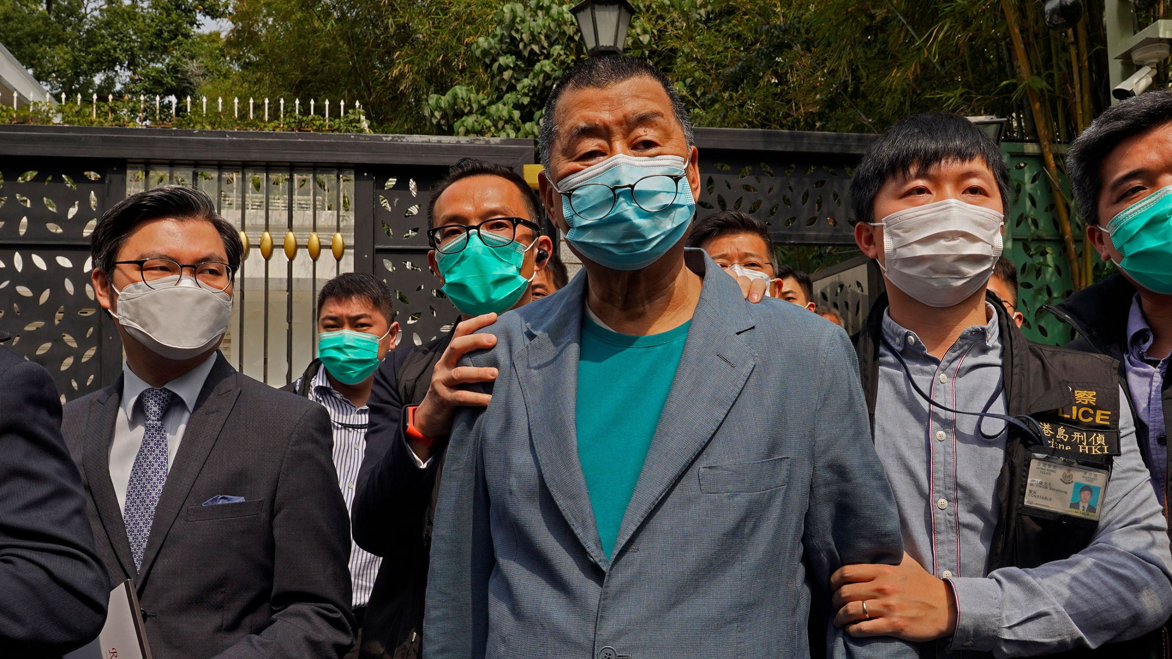 Hong Kong media tycoon Jimmy Lai, is arrested by police officers at his home in Hong Kong, April 18, 2020. Jimmy Lai is shown being held by security officials while wearing a blue blazer and a face mask.