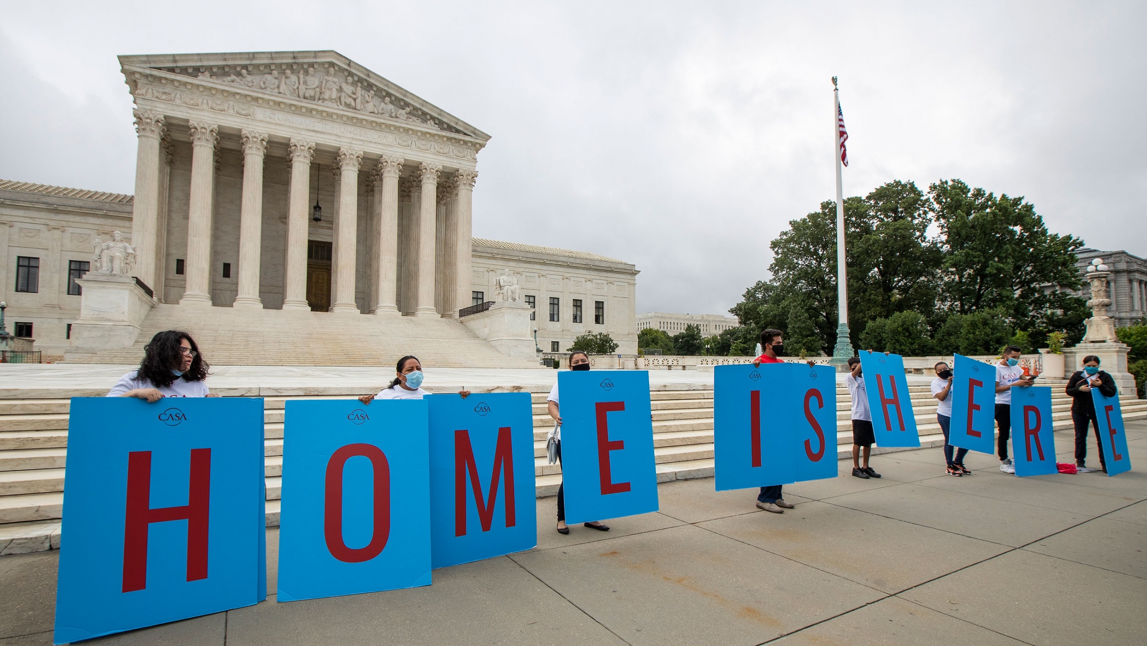 Deferred Action for Childhood Arrivals (DACA) students gather in front of the Supreme Court in Washington, June 18, 2020. Several people are shown standing behind large placards that together spell out, "Home is here."