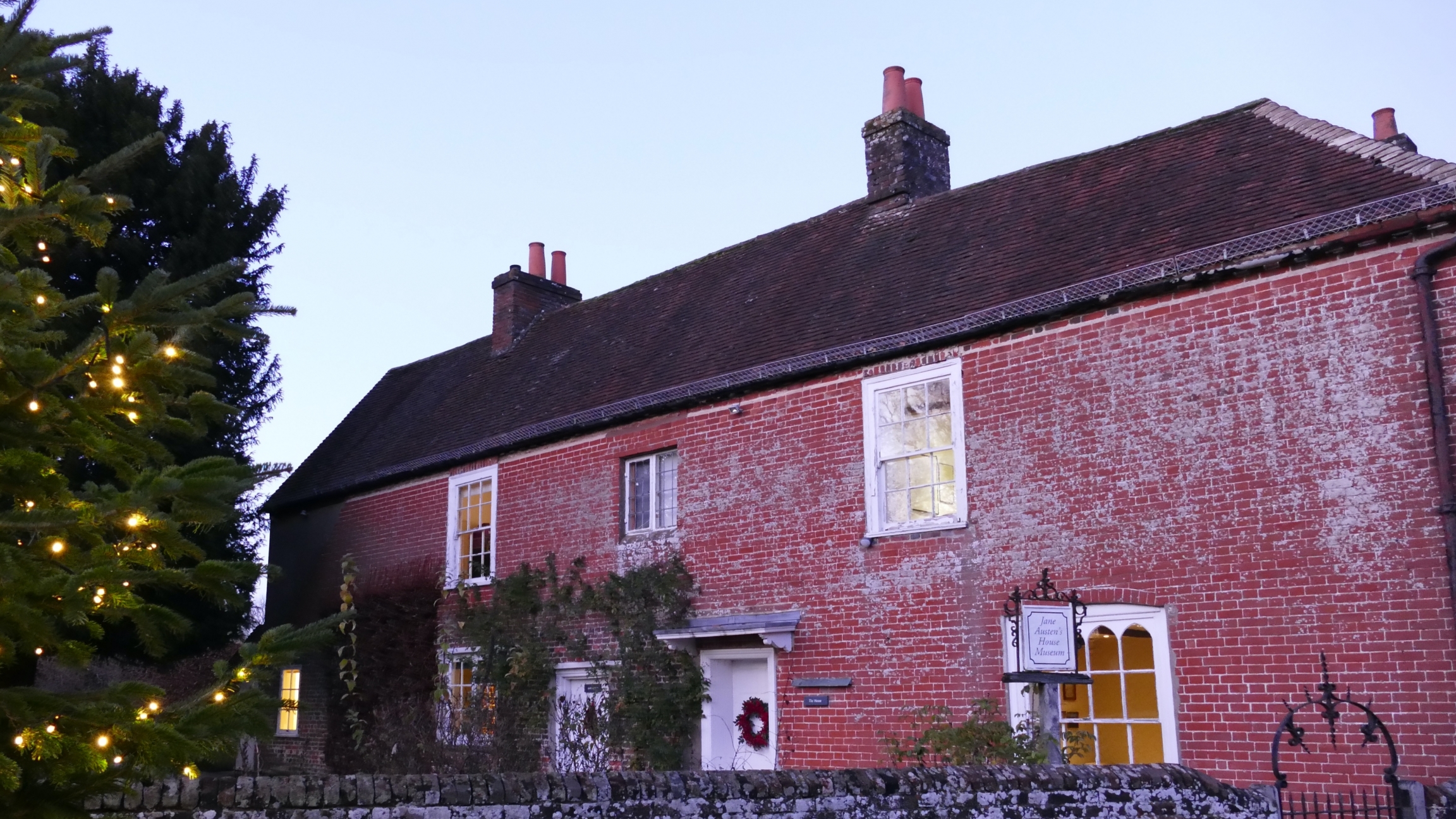 Jane Austen's house in the United Kingdom. A red brick house next to a tree with Christmas lights