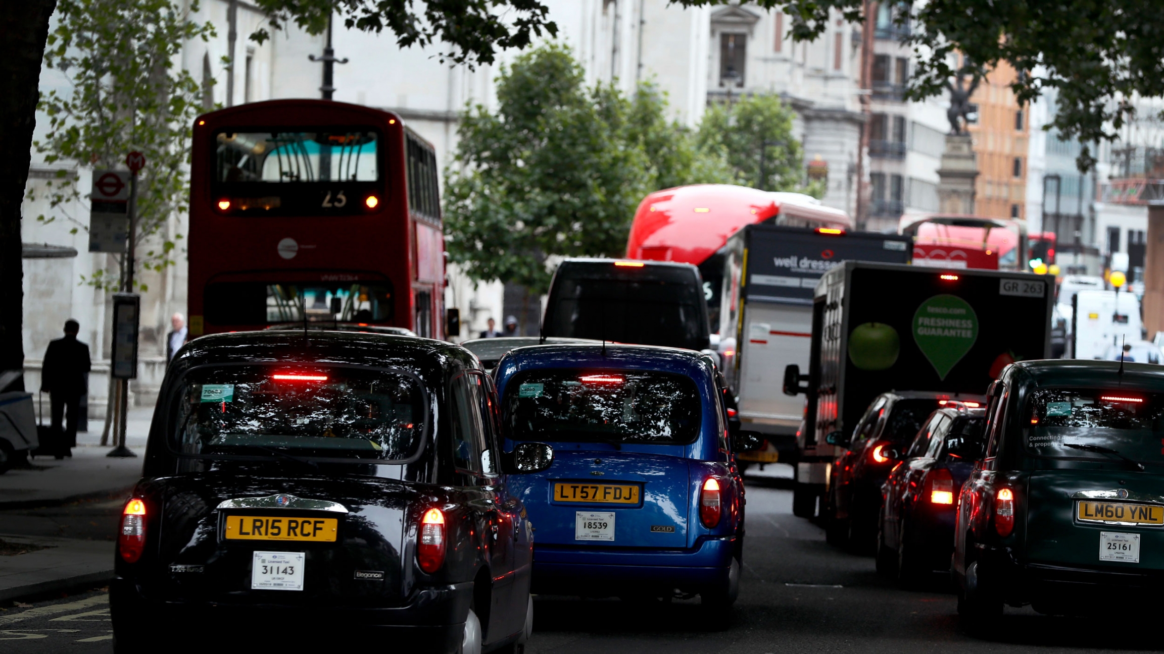 Vehicles drive on a congested London street, 2017. Several vehicles are shown bumper to bumper congested street.