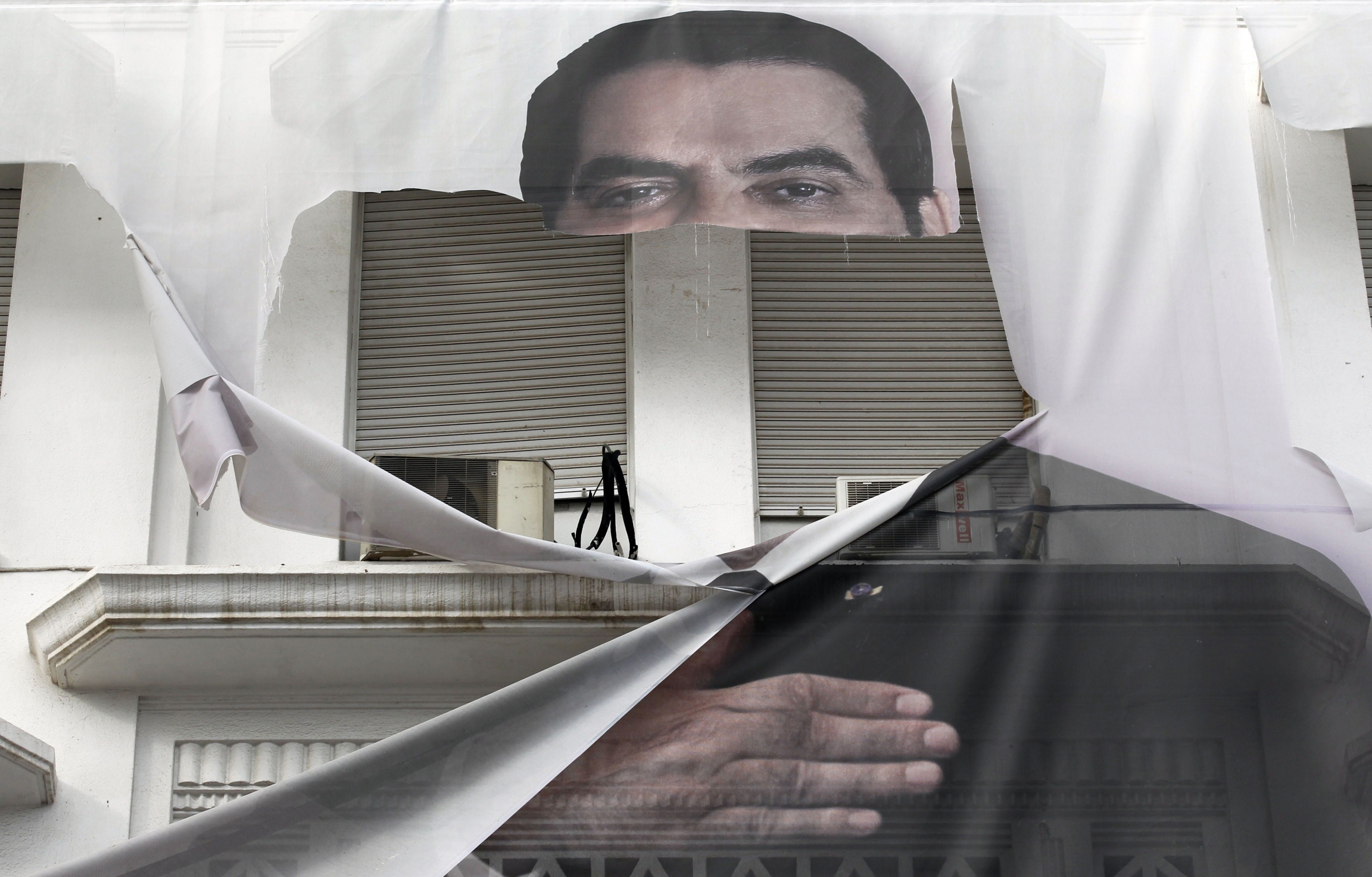 In this Jan.16, 2011 file photo, a torn banner of former Tunisian President Zine El Abidine Ben Ali is seen in the center of Tunis.