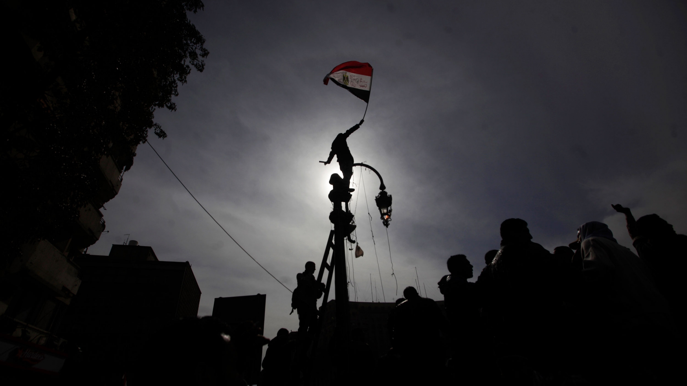 A protester climbs a pole waving the Egyptian national flag during a demonstration in Tahrir Square, Cairo, Egypt, Feb. 3, 2012. A protester is shown standing on top of a street light and holding the Egyptian flag while blocking the sun and creating a shadow.