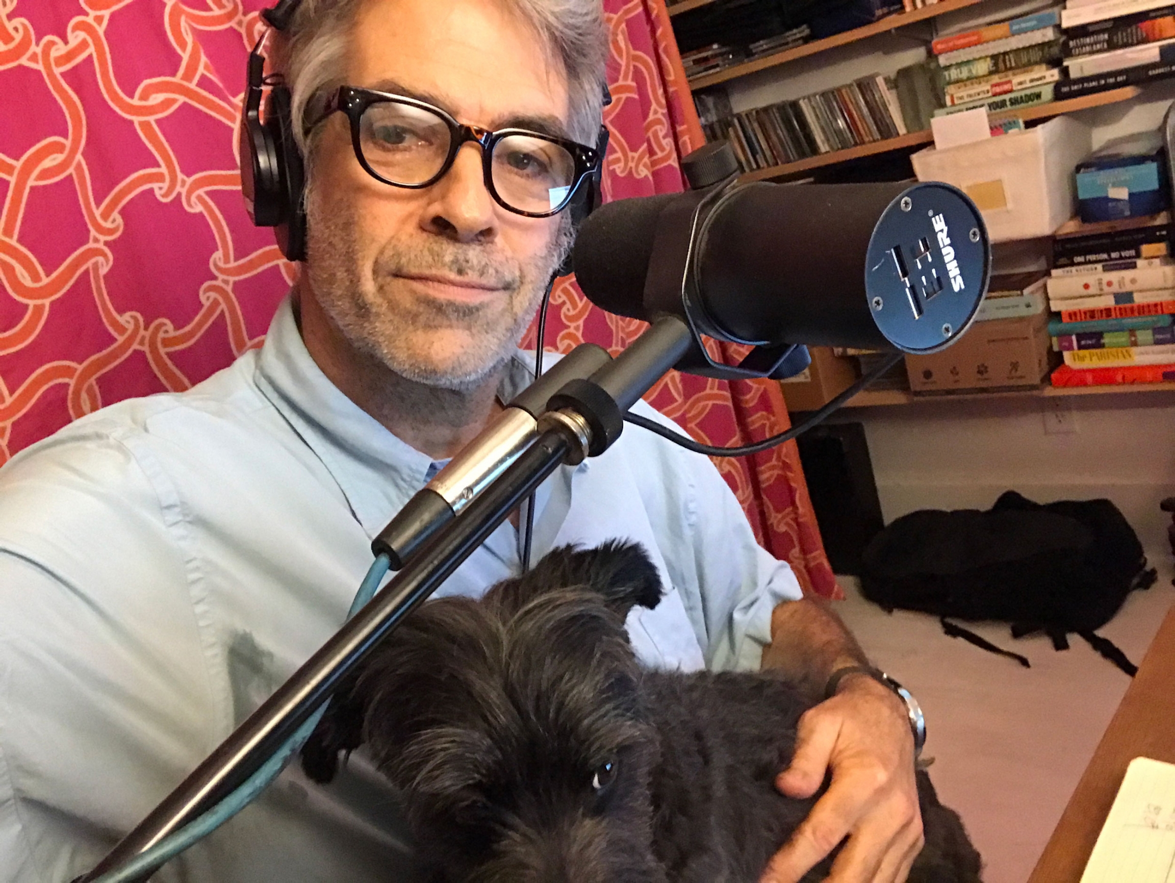 The World's host Marco Werman and his dog Frankie getting ready to host the show from home. Marco Werman is shown with a microphone and his dog Frankie sitting on his lap.