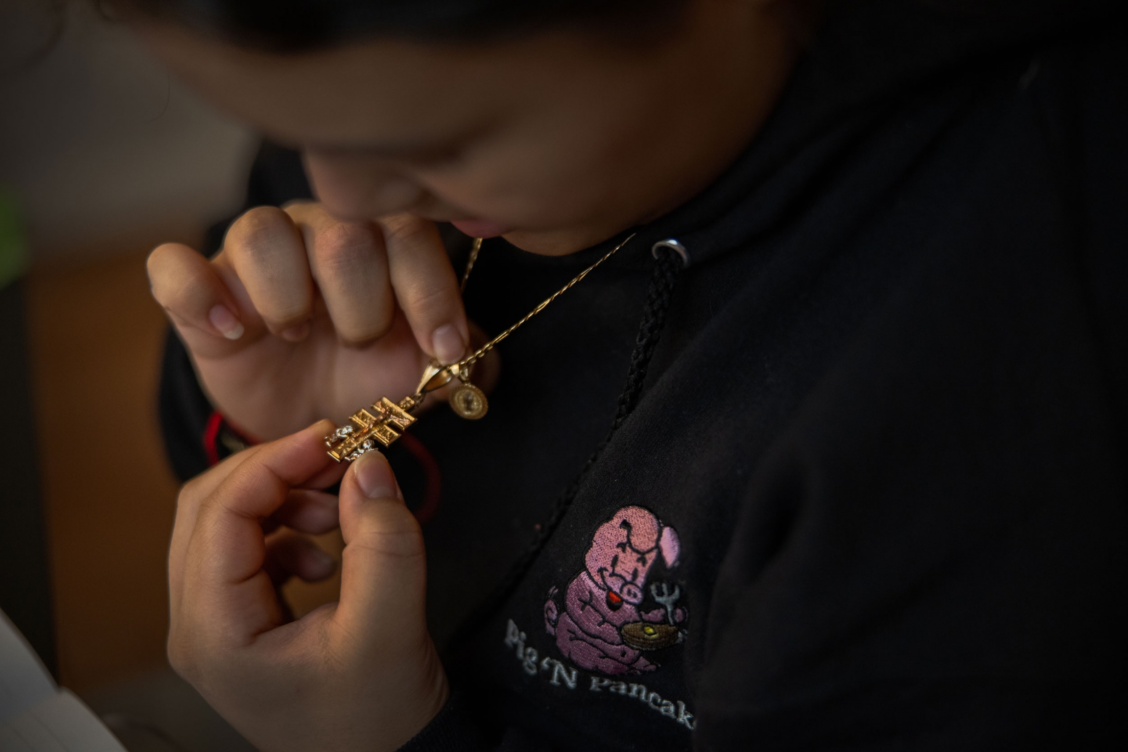 Michelle Aguilar Ramirez looks at a cross called the Caravaca de la Cruz, which she says she wears to bring good fortune and inner peace, at her home in Spokane, Washington. A woman is shown looking down at a golden cross hanging from her neck.