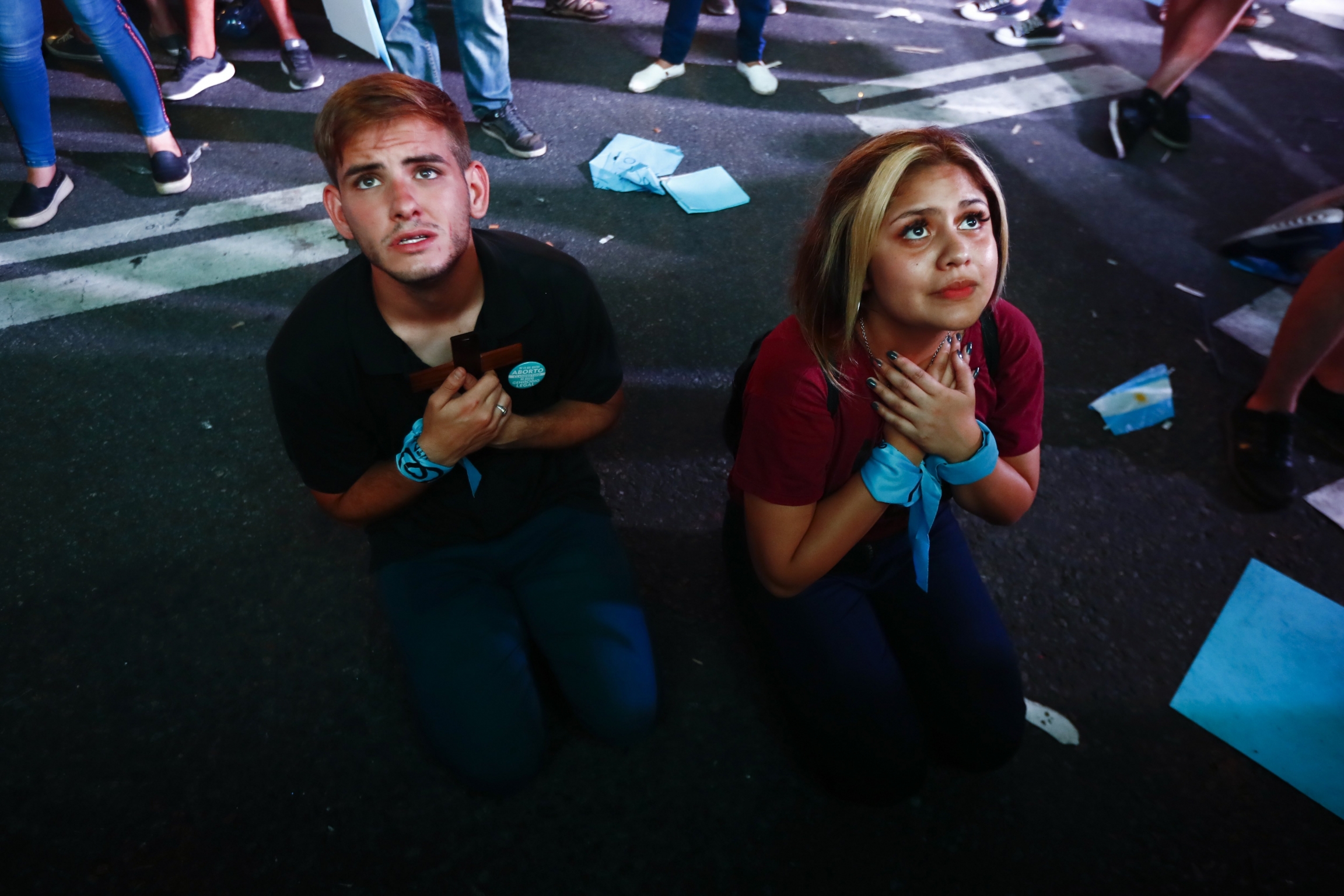 Anti-abortion activists pray during a demonstration against the decriminalization of abortion as lawmakers debate its legalization, outside Congress in Buenos Aires, Argentina, on Tuesday, Dec. 29, 2020. A young man and a young woman, wearing a blue scarf around their wrist, kneel down to pray on the street.