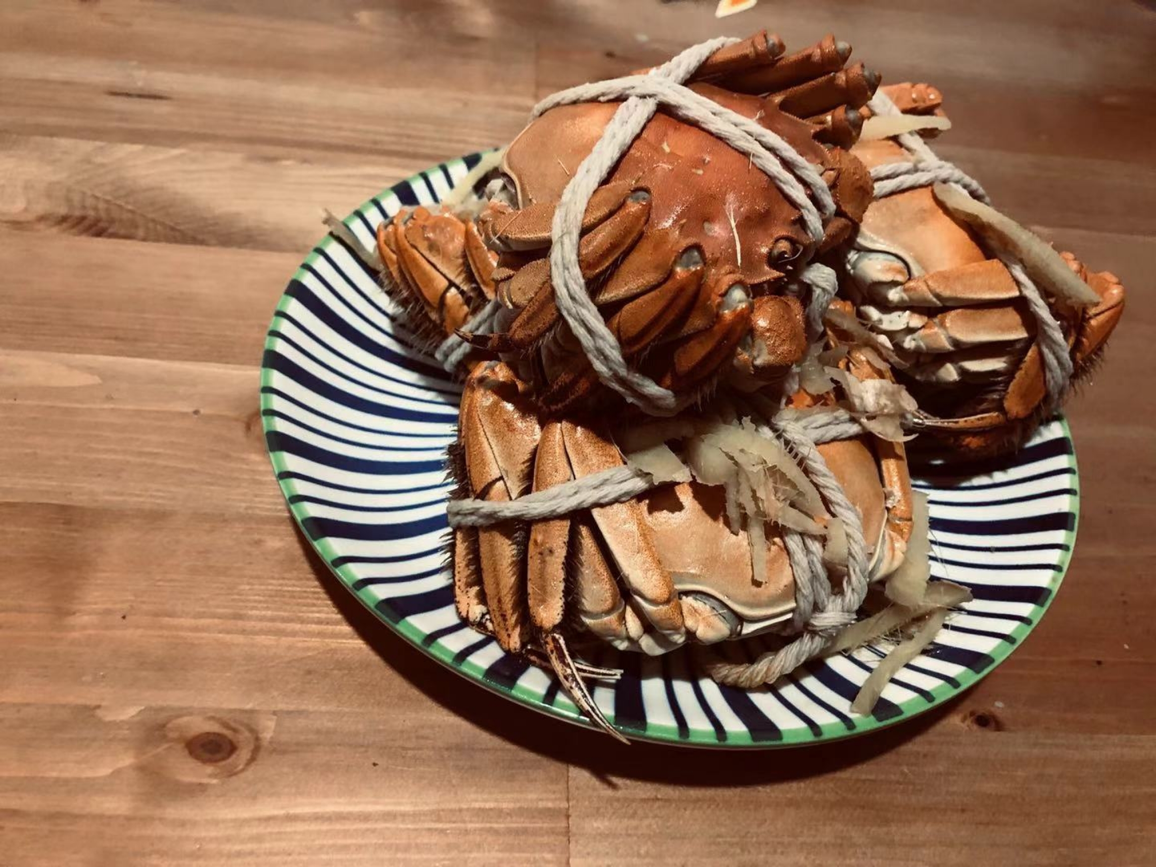 A plate of hairy crabs. A couple of hairy crabs are shown tied together with a rope and sitting on a striped plate.
