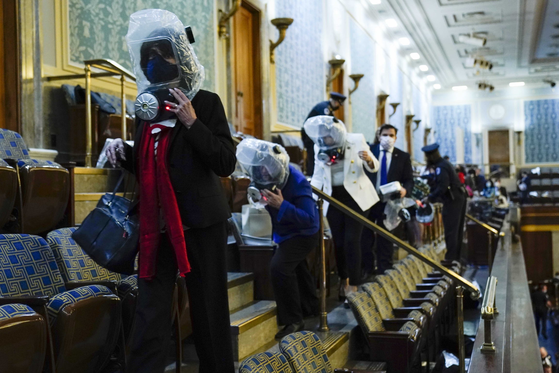People shelter in the House gallery as a mob of Trump supporters try to break into the House Chamber at the U.S. Capitol on Wednesday, Jan. 6, 2021, in Washington, DC. People wearing plastic protection around their heads shelter in the House gallery as a mob of Trump supporters try to break into the House chamber at the US Capitol on Wednesday, Jan. 6, 2021, in Washington, DC.
