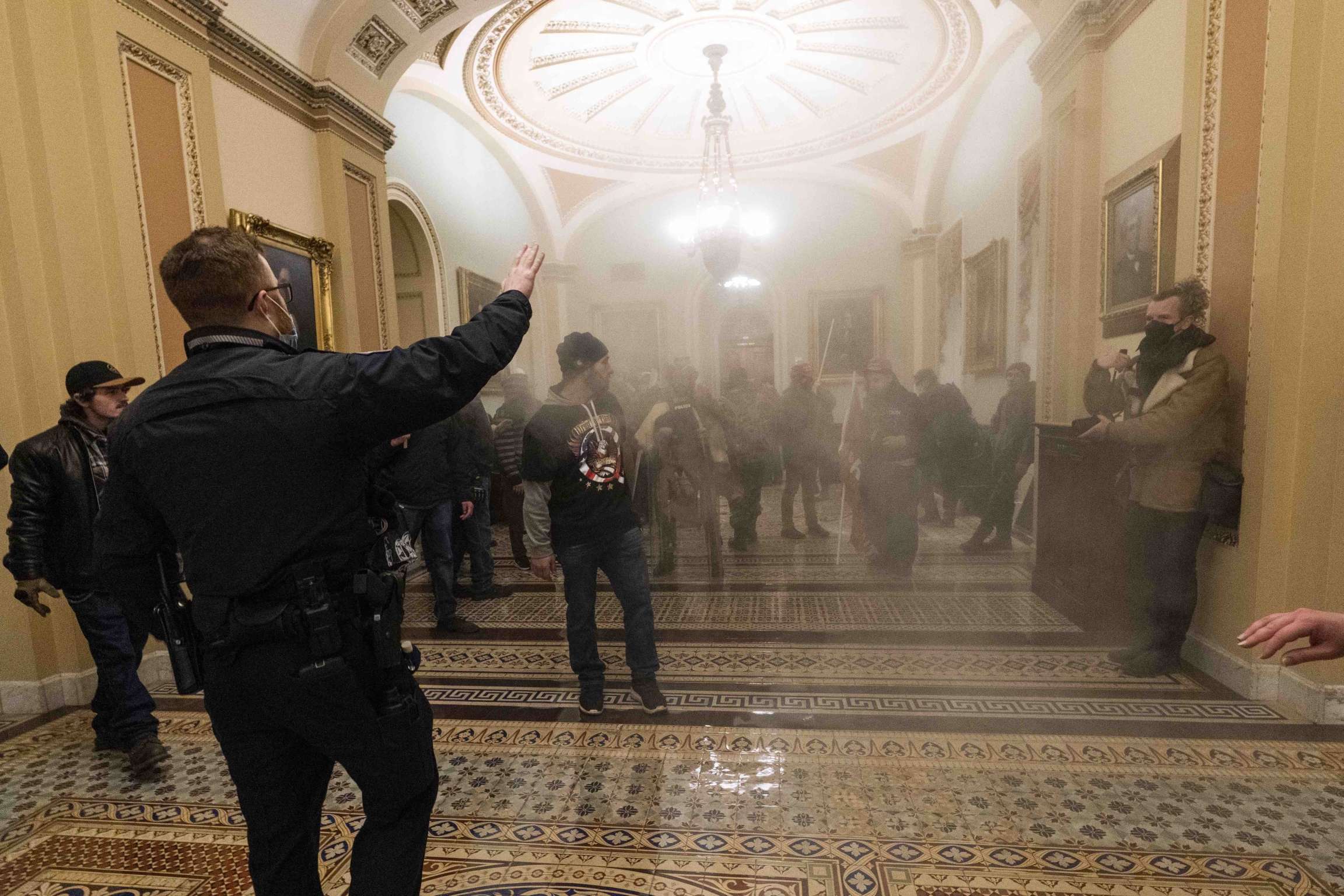 Smoke fills the walkway outside the Senate chamber as supporters of President Donald Trump are confronted by US Capitol Police officers inside the Capitol, Wednesday, Jan. 6, 2021, in Washington, DC. Smoke fills the walkway outside the Senate chamber as supporters of President Donald Trump are confronted by US Capitol Police officers inside the Capitol, Wednesday, Jan. 6, 2021, in Washington, DC.