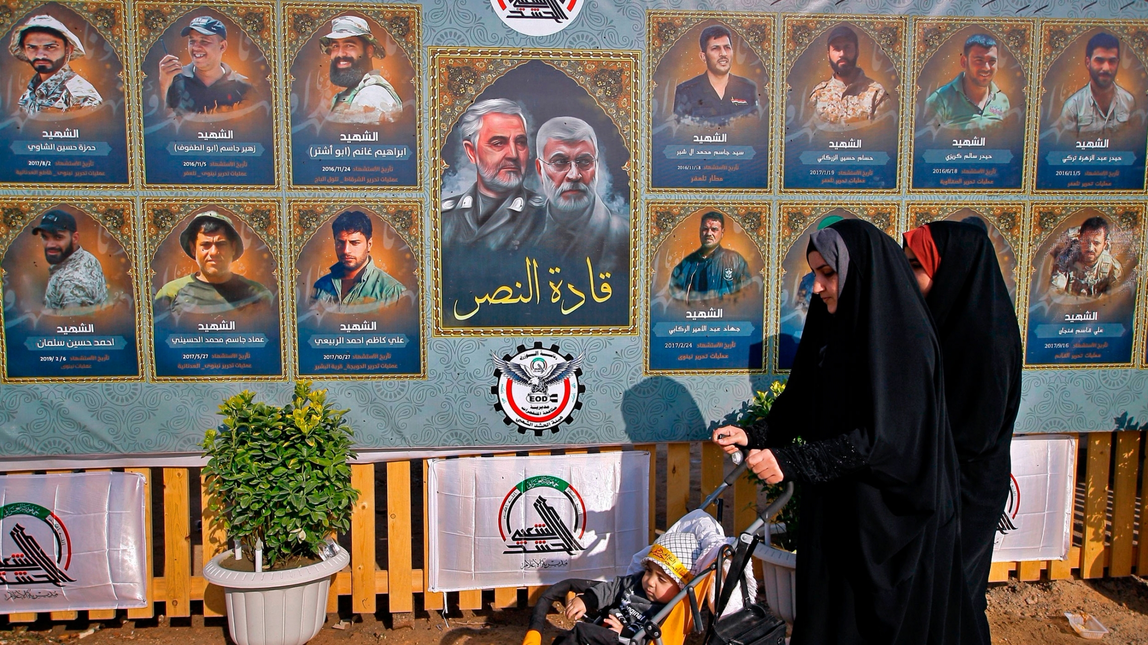 People pass by posters of Gen. Qassem Soleimani, center left, head of Iran's Quds force and fighters killed in fighting during the anniversary procession in the cemetery in Najaf, Iraq, Jan. 4, 2021. People pass by posters of Gen. Qassem Soleimani along with several other illustrated portraits alongside.