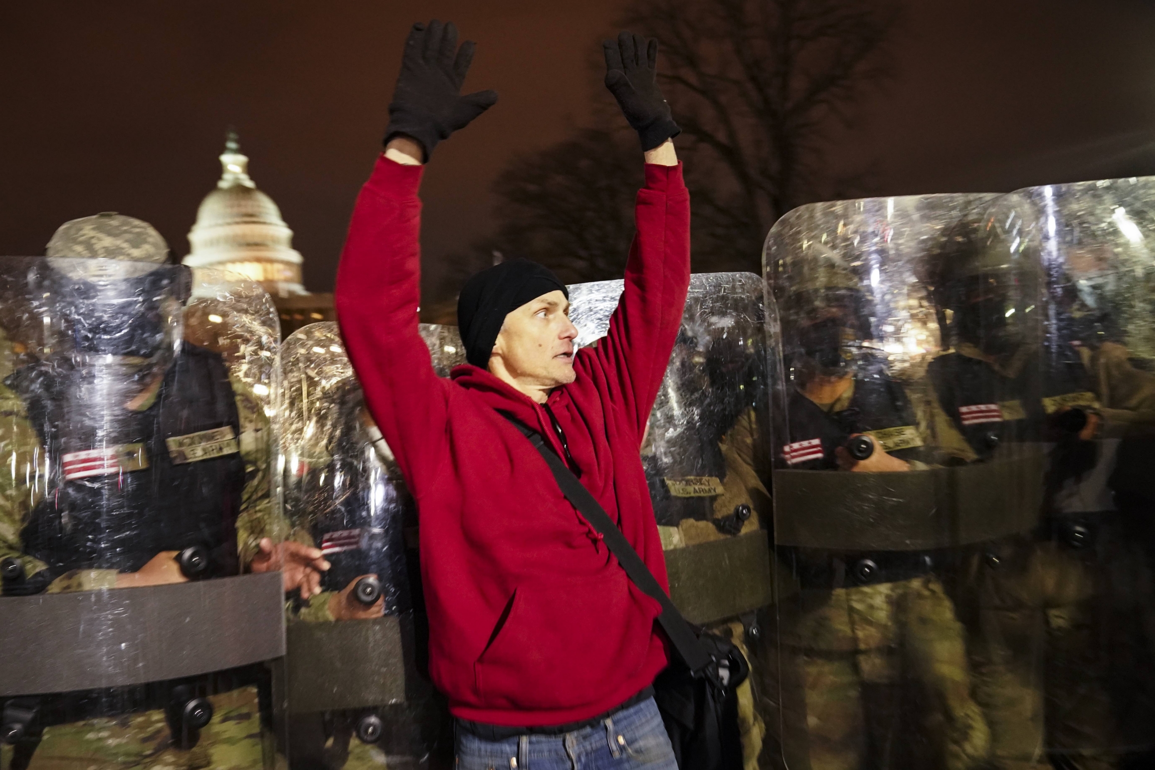 The DC National Guard moves a demonstrator outside the Capitol on Wednesday night, Jan. 6, 2021, after a day of rioting. National guard appear behind a man wearing a red sweater, who has his hands up.