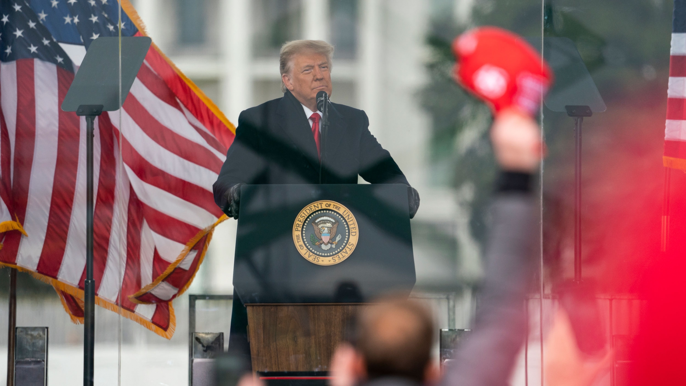 President Donald Trump speaks during a rally protesting the electoral college certification of Joe Biden as President, Wednesday, Jan. 6, 2021, in Washington. President Donald Trump is shown standing at a podium speaking with US flags waving behind him.