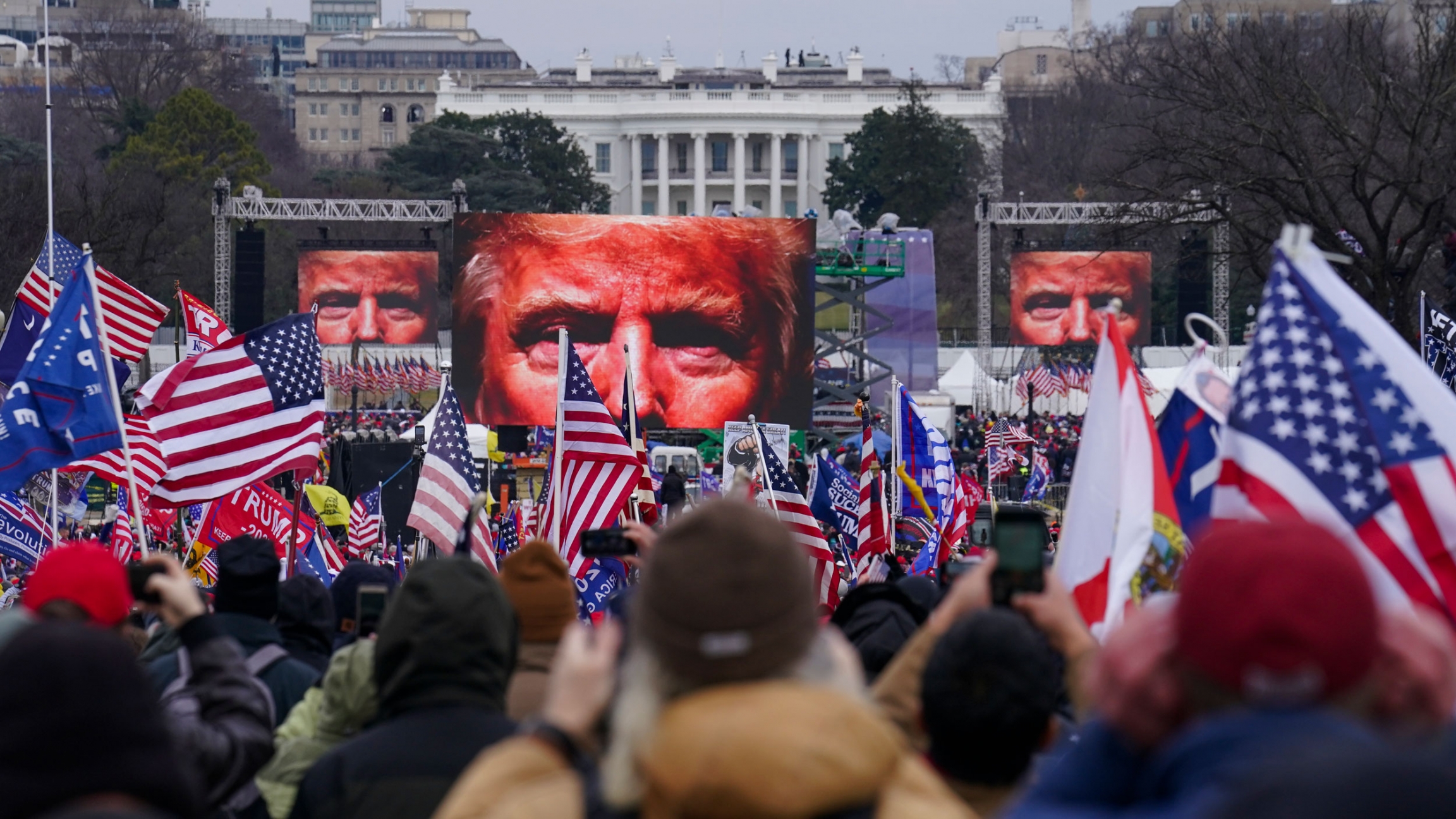US President Donald Trump supporters participate in a rally in Washington. Far-right social media users for weeks openly hinted in widely shared posts that chaos would erupt at the US Capitol while Congress convened to certify the election results, Jan. 6 A large crowd of people are shown holding small US flags with screens showing Donald Trump's eyes in the distance.