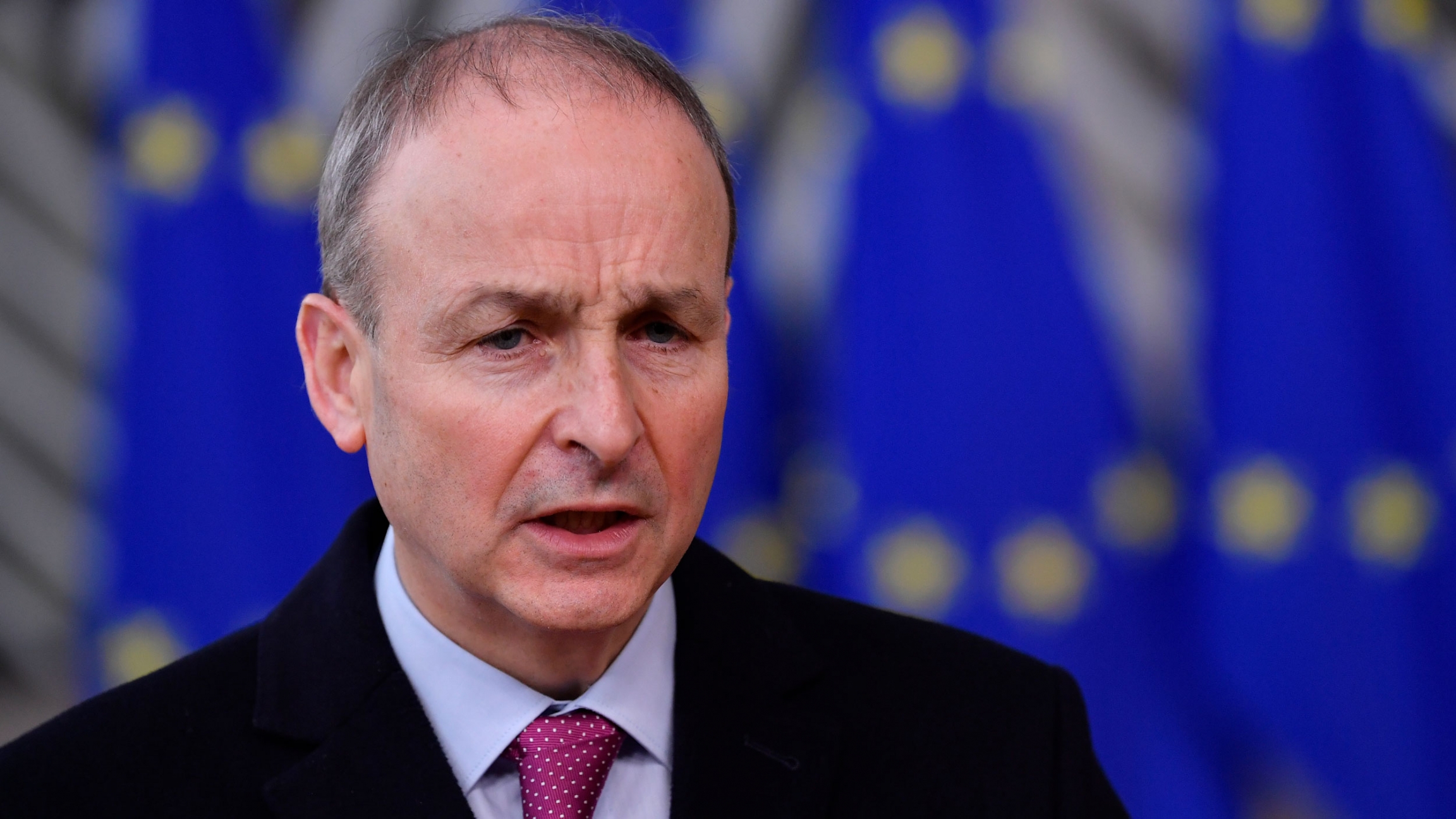 Ireland's Prime Minister Micheal Martin speaks at the European Council building in Brussels, Dec. 2020. Ireland's Prime Minister Micheal Martin is shown wearing a dark suit jacket and red tie.