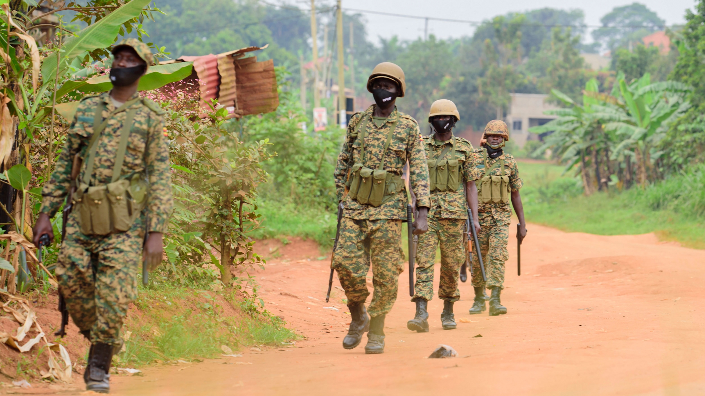 Soldiers patrol outside opposition challenger Bobi Wine's home in Magere, Kampala, Uganda, after President Yoweri Museveni was declared the winner of the presidential election, Jan. 16, 2021. Four soldiers are shown wearing military fatigues and helmets while carrying weapons and walking in a dirt road.