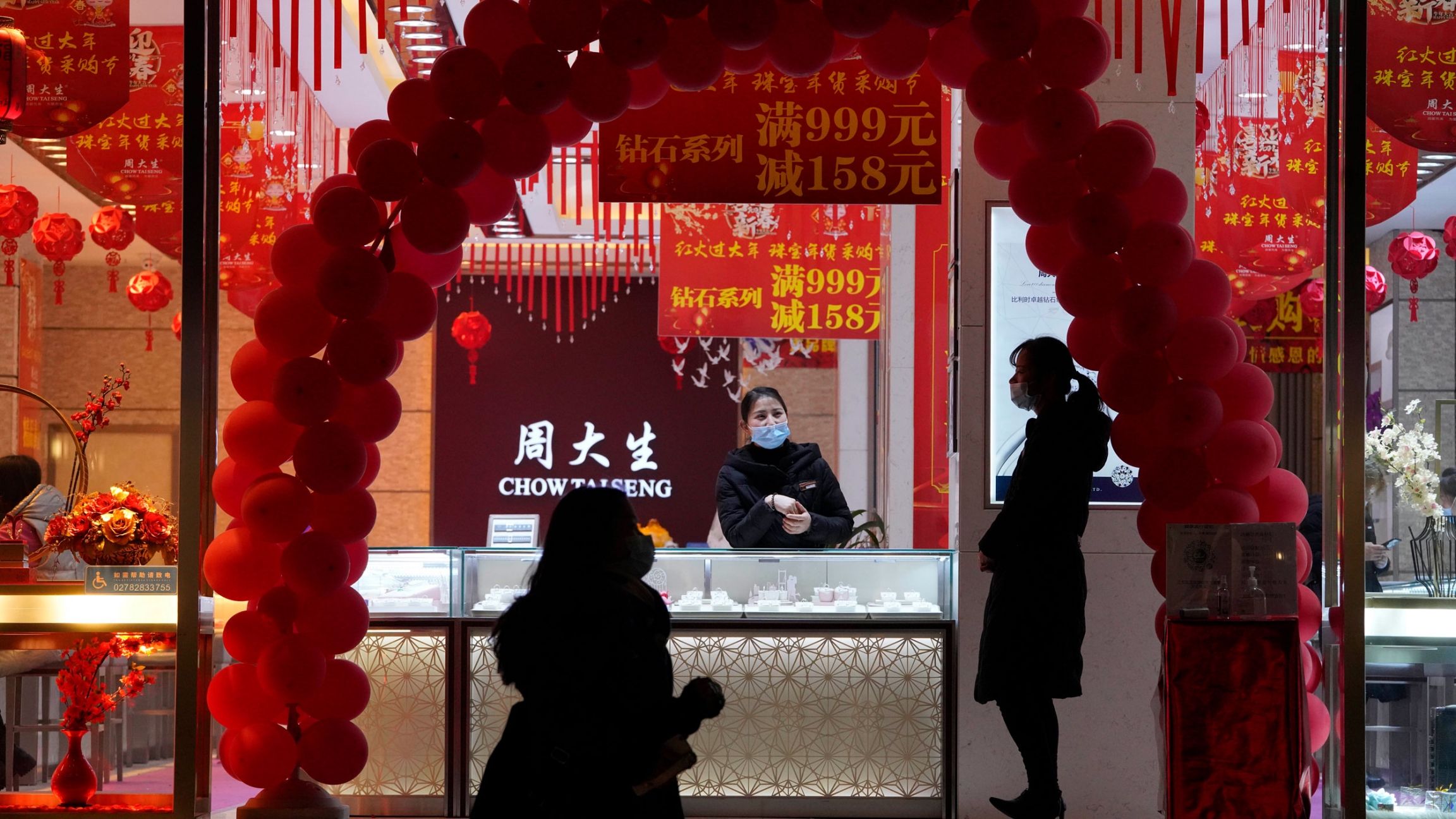 Workers wearing masks at a jewelry shop waits for customers in Wuhan in central China's Hubei province, Jan. 14, 2021. The the front window of jewelry store is shown framed by an arc of red balloons.