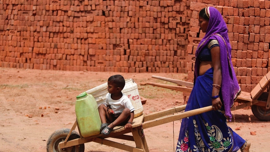 An Indian woman pushes a cart with her child as she works at a brick kiln during lockdown to curb the spread of new coronavirus on the outskirts of Jammu, India, Sunday, May 10, 2020. A woman pushes a wheelbarrow with a child riding on it.
