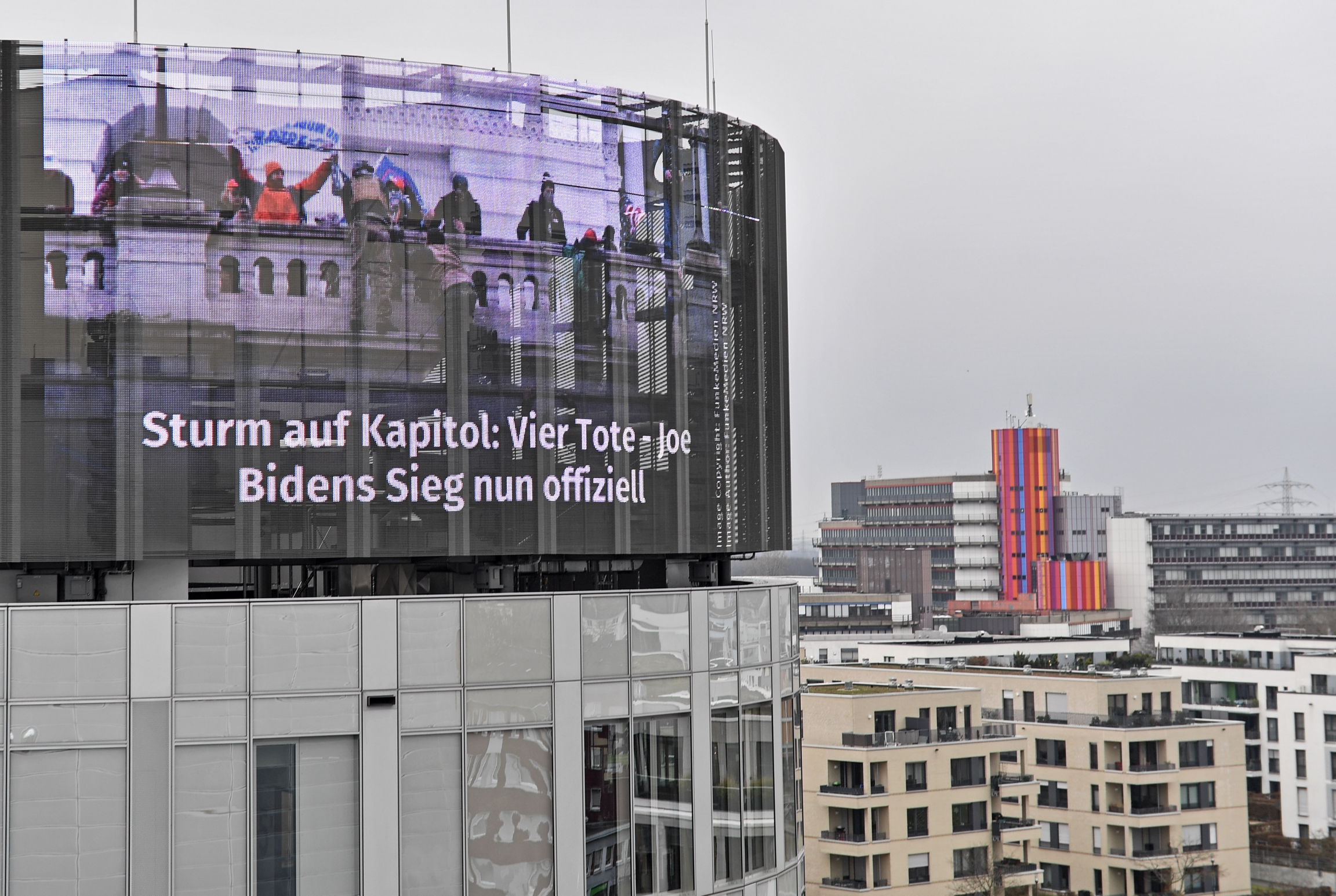 A big news screen on a building in Essen, Germany, showing protesters on the US Capitol in Washington, a headline reads 