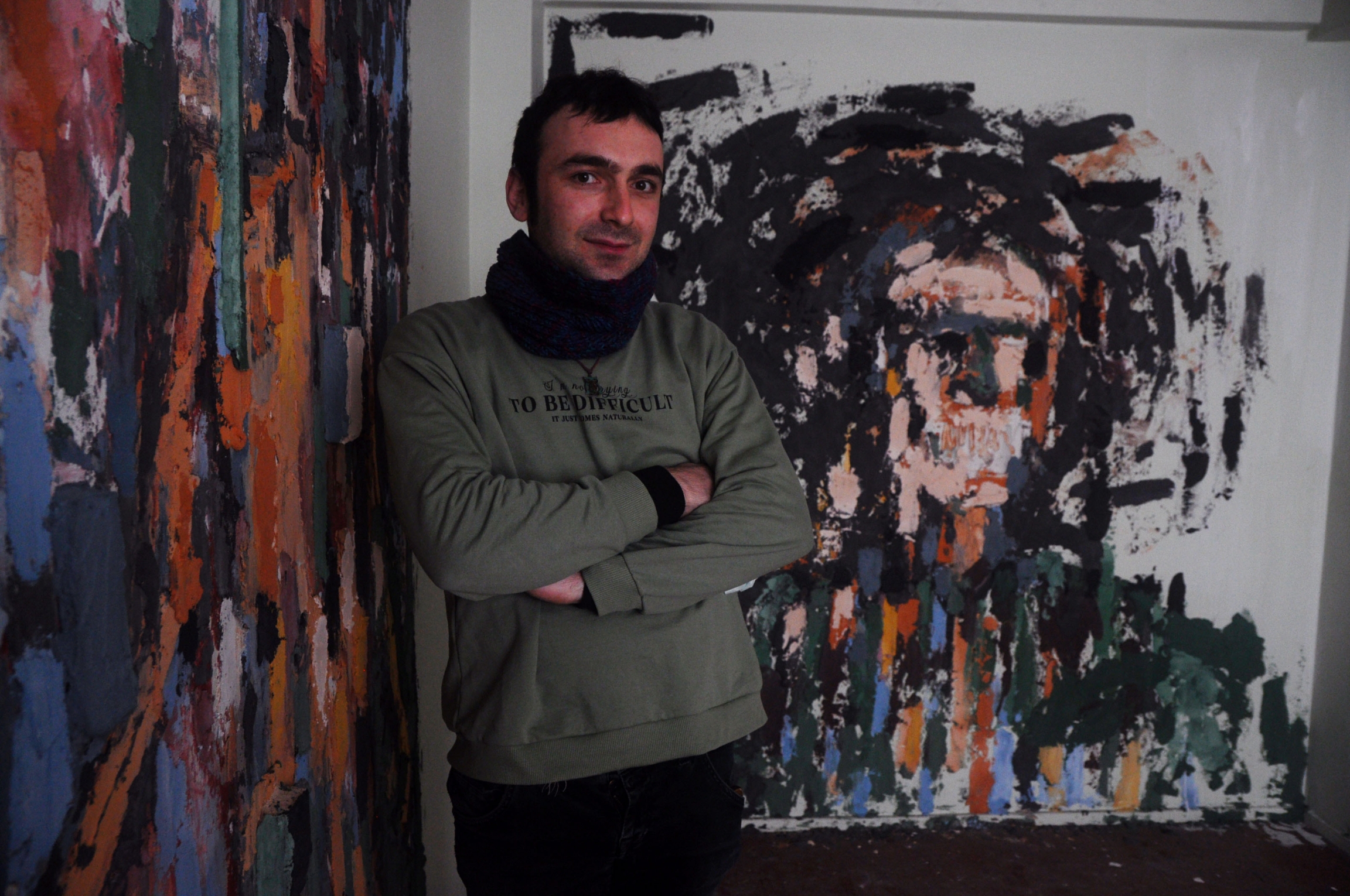 Batikan Bostanci, 30, stands with his installation, “Powerless Faces.” Bostanci layered pigments and paint over textured concrete, wood and plastic remnants found in the debris left by the building’s residents. Batikan Bostanci, 30, stands with his installation, “Powerless Faces.” Bostanci layered pigments and paint over textured concrete, wood and plastic remnants found in the debris left by the building’s residents.
