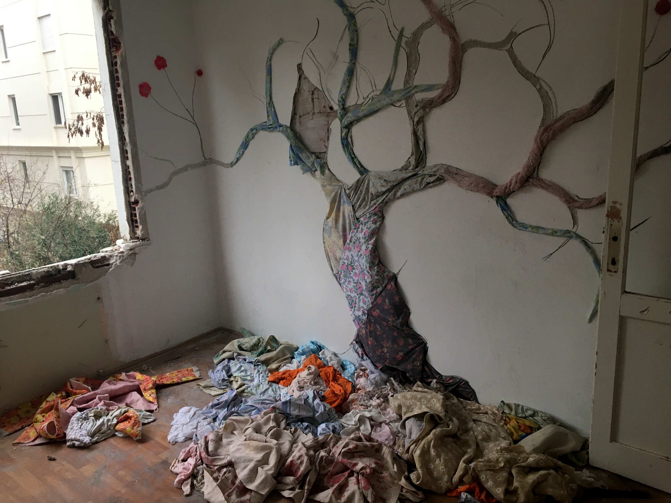 A tree made of found fabrics pinned to a wall by Songul Girgin gazes wistfully out of what was once a bedroom window. A tree made of found fabrics pinned to a wall by Songul Girgin gazes wistfully out of what was once a bedroom window.