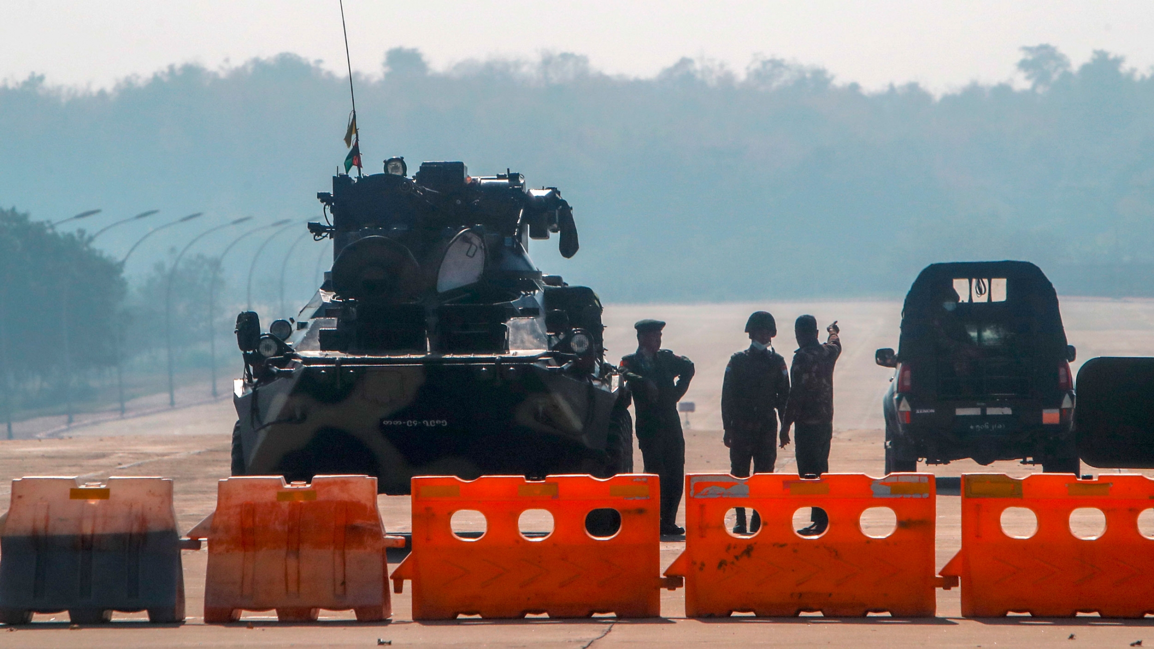 Myanmar's military stand guard at a checkpoint manned with an armored vehicle in a road leading to the parliament building a day after Myanmar’s military staged a coup, Naypyitaw, Myanmar, Feb. 2, 2021. Several military personale are shown standing next to a tank with orange road blocks lined up across as road.