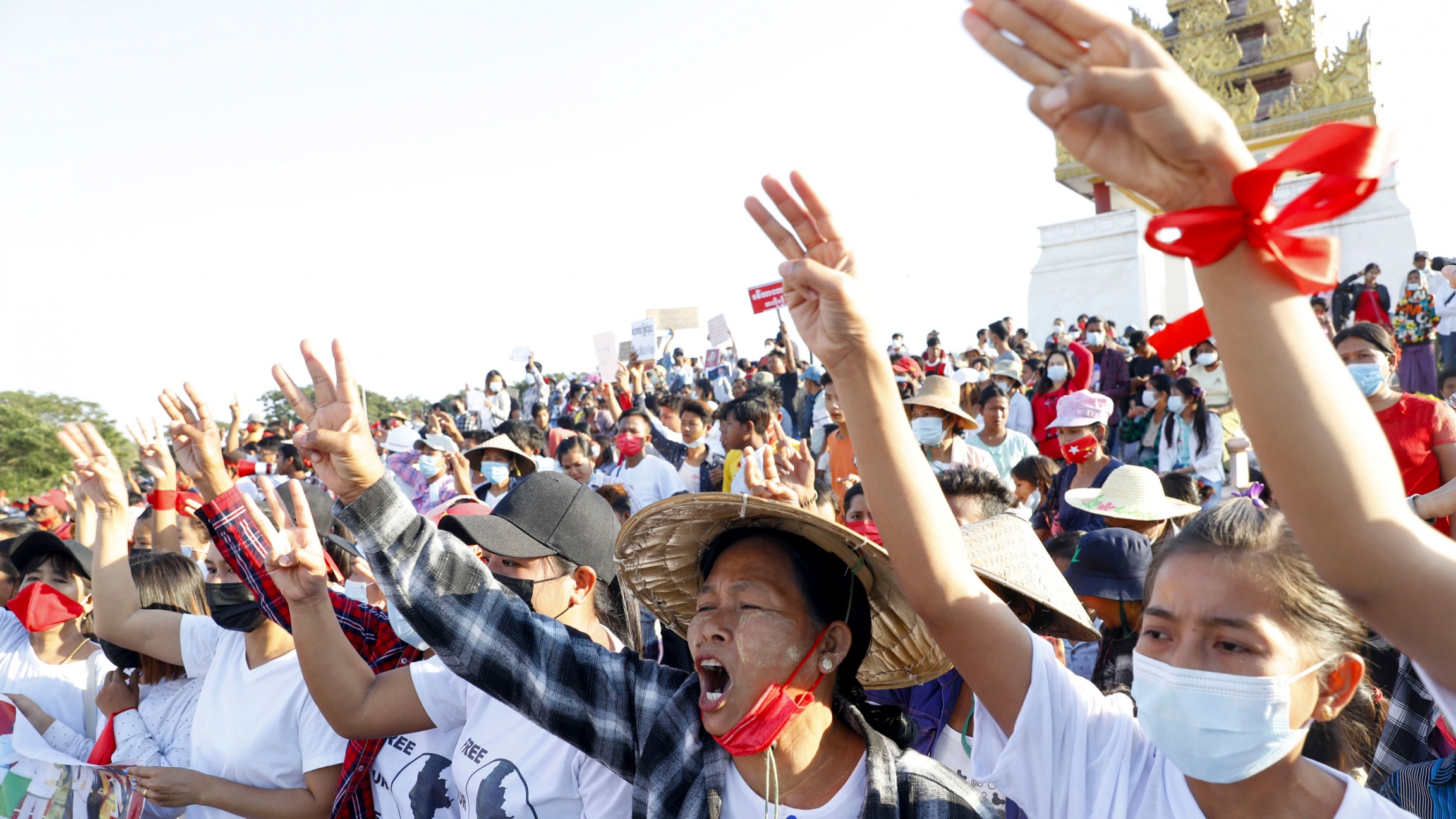 Demonstrators flash three-fingered salutes, a symbol of resistance, against the military coup and shout slogans calling for the release of detained Myanmar leader Aung San Suu Kyi during a protest in Mandalay, Myanmar, Feb. 10, 2021. A large crowd of people are shown, many with their hands raise and holding three fingers in the air with a golden-color shrine seen in the distance.