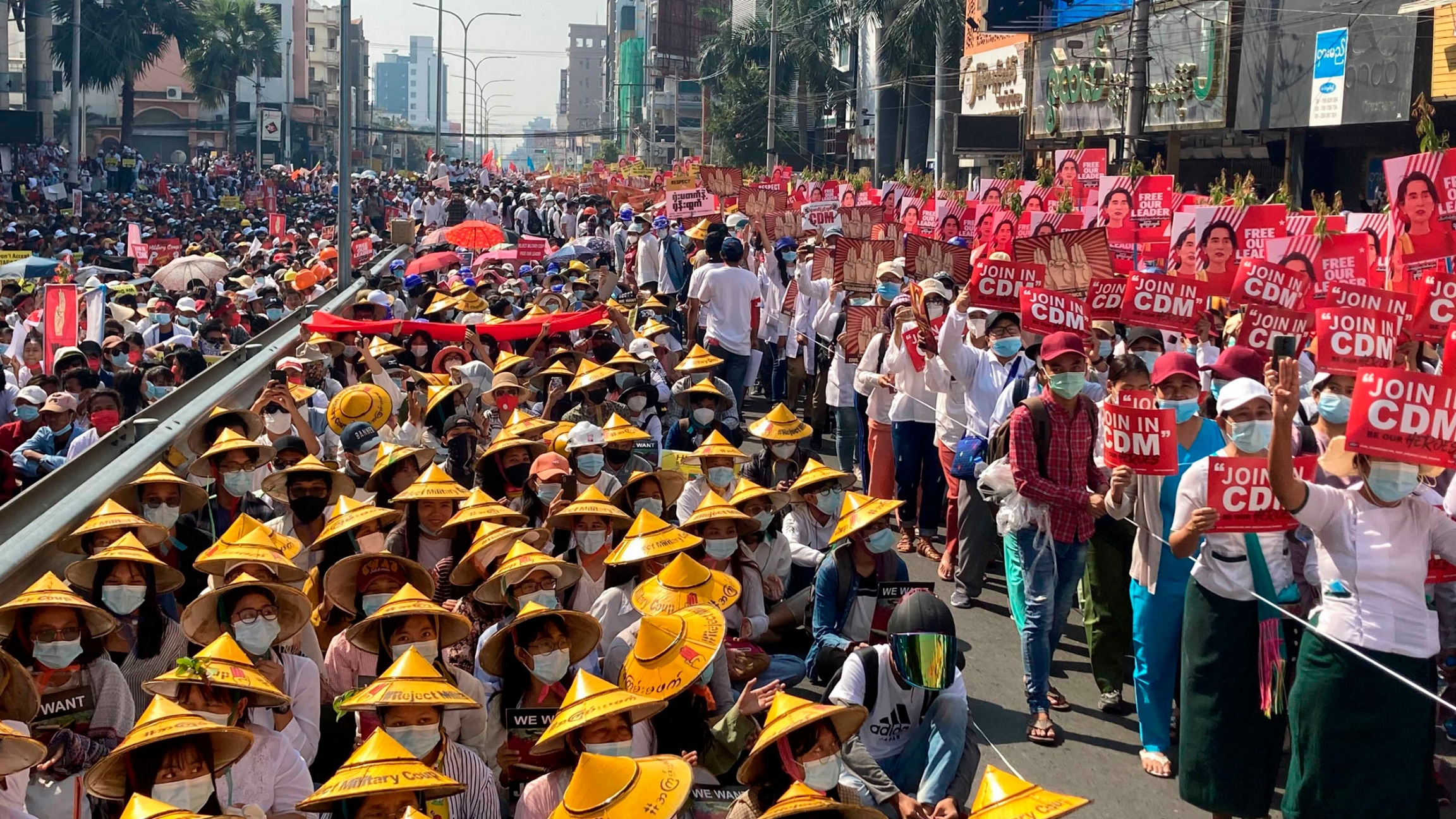 Anti-coup protesters fill the main road during a rally in Mandalay, Myanmar, Feb. 22, 2021. A large crowd of people are shown filling a street with many wearing traditional Asian hats and carrying red signs.