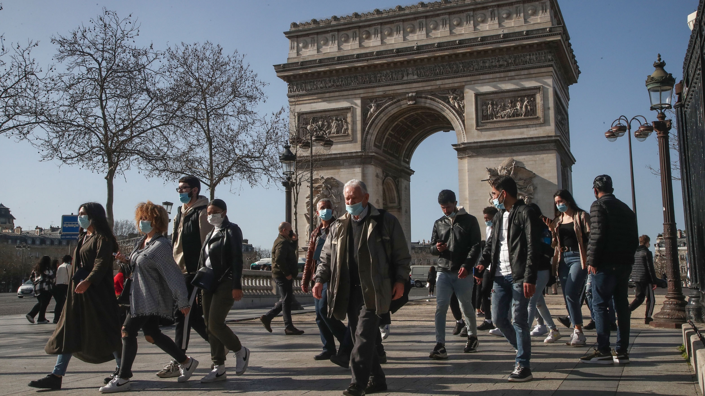 People wearing wearing face masks to prevent the spread of coronavirus make their way at the Champs-Elysees avenue in Paris, Feb. 24, 2021. A crowd of people are shown walking with Paris' iconic Arc de Triomphe in the background.