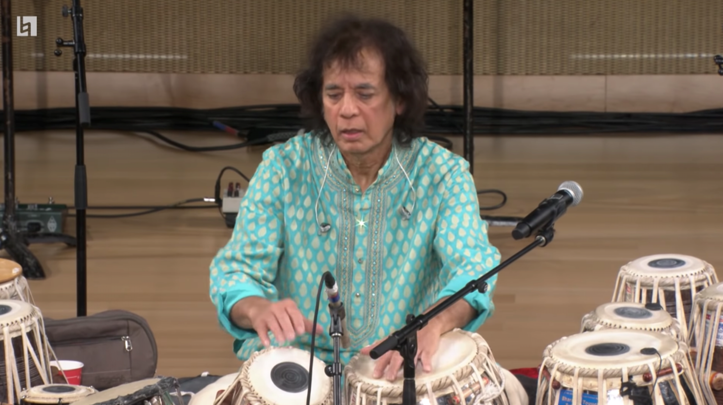 Zakir Hussain plays tabla. A man plays tabla while wearing a light blue shirt.