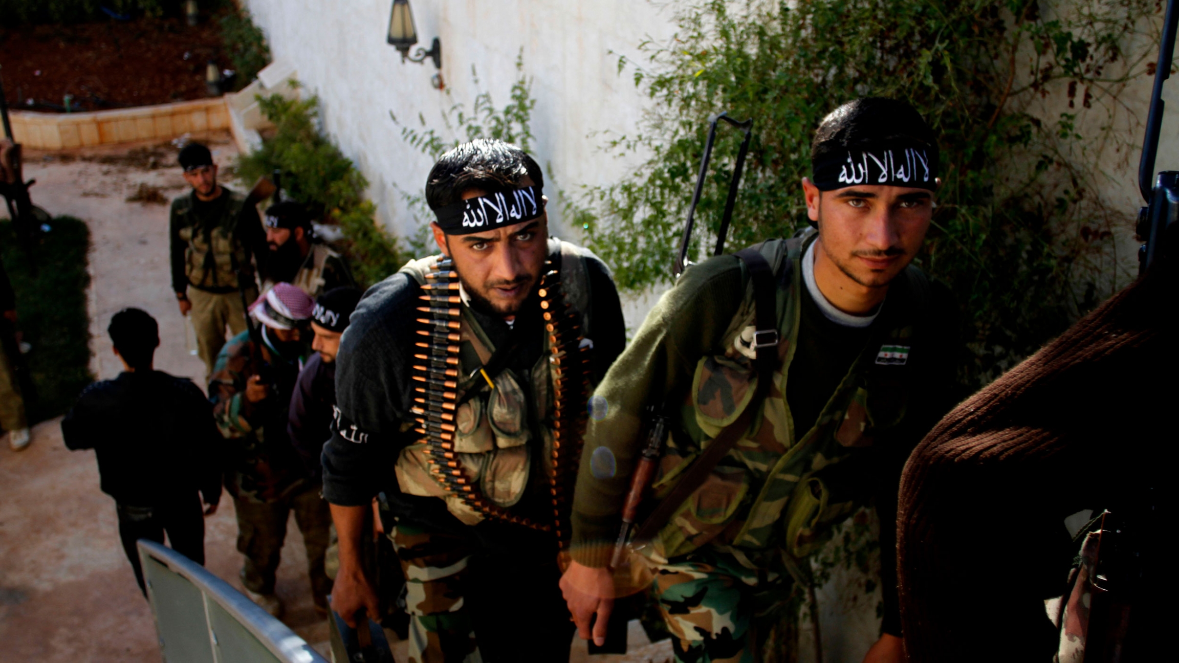 Syrian fighters of The Beloved of Allah brigade hold their weapons before fighting with government forces on the outskirts of Aleppo, Nov. 2012. Several men are shown wearing military fatigues and carrying weapons while walking up a staircase.