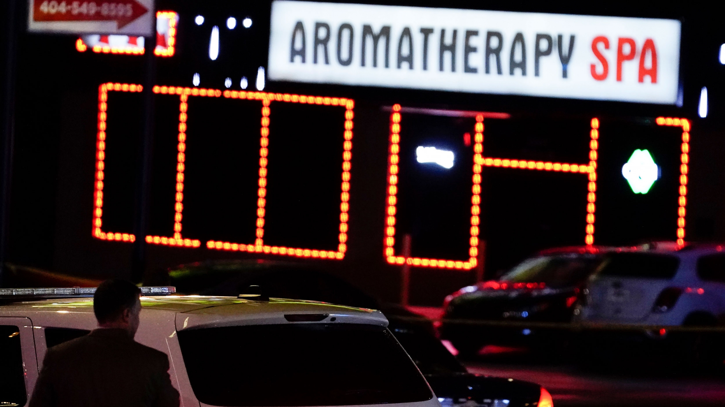 Police officials stand in front of a spa after a shooting, in Atlanta, Georgia, March 16, 2021. A police SUV is shown in the nearground with a bright white sign in the distance for an Aromatherapy spa.
